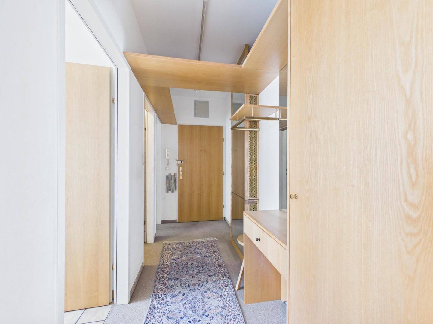 Eingangsbereich mit Garderobe, Teppichboden und Holztür.