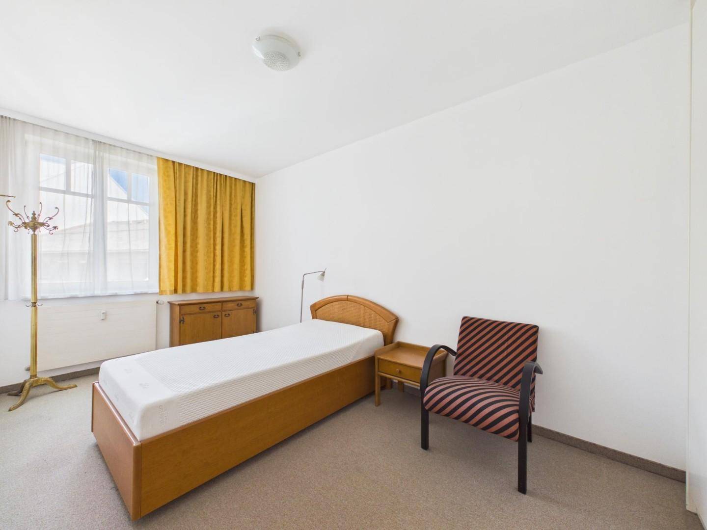 Helles Schlafzimmer mit Einzelbett, gelben Vorhängen und Teppichboden.