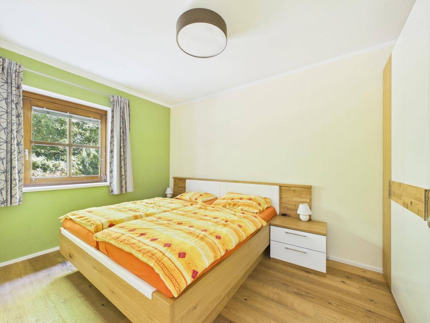 Helles Schlafzimmer mit Doppelbett, Holzmöbeln und freundlichen grünen Wänden.