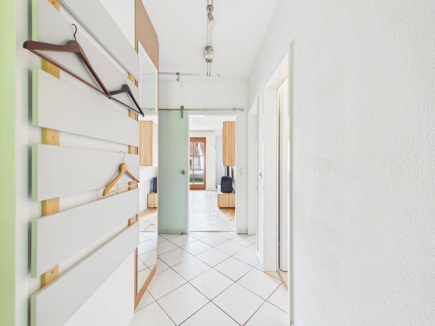 Heller Flur mit weißen Fliesen, moderner Garderobe und Schiebetür zu den Wohnbereichen.