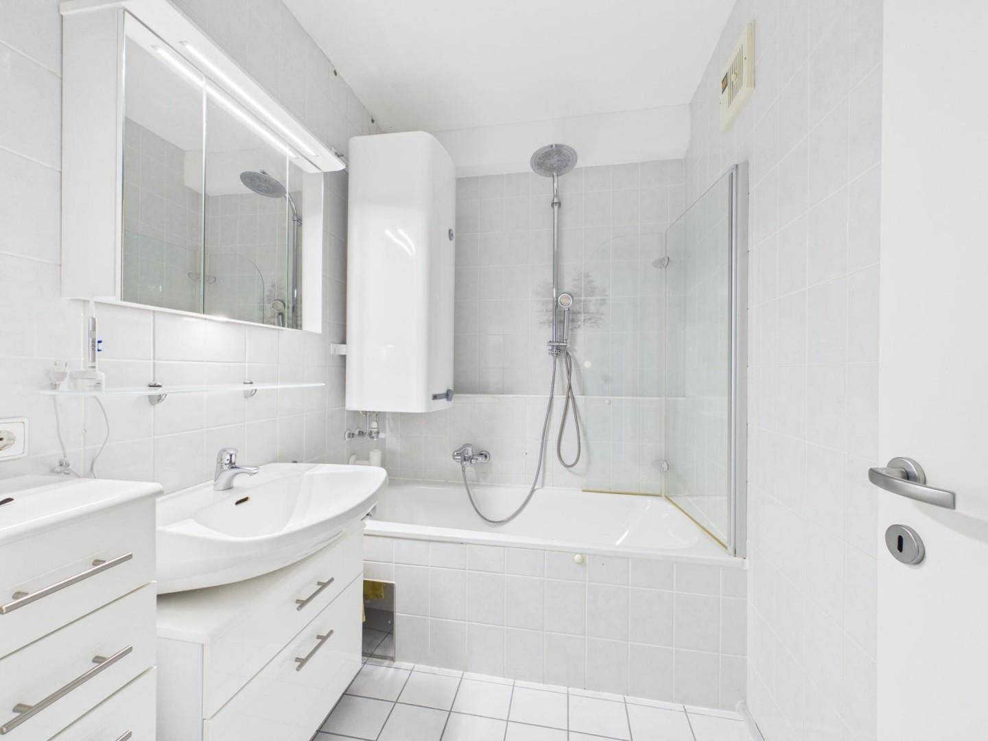 Funktionales Badezimmer mit Badewanne, Dusche, Waschbecken und Spiegelschrank, komplett gefliest.