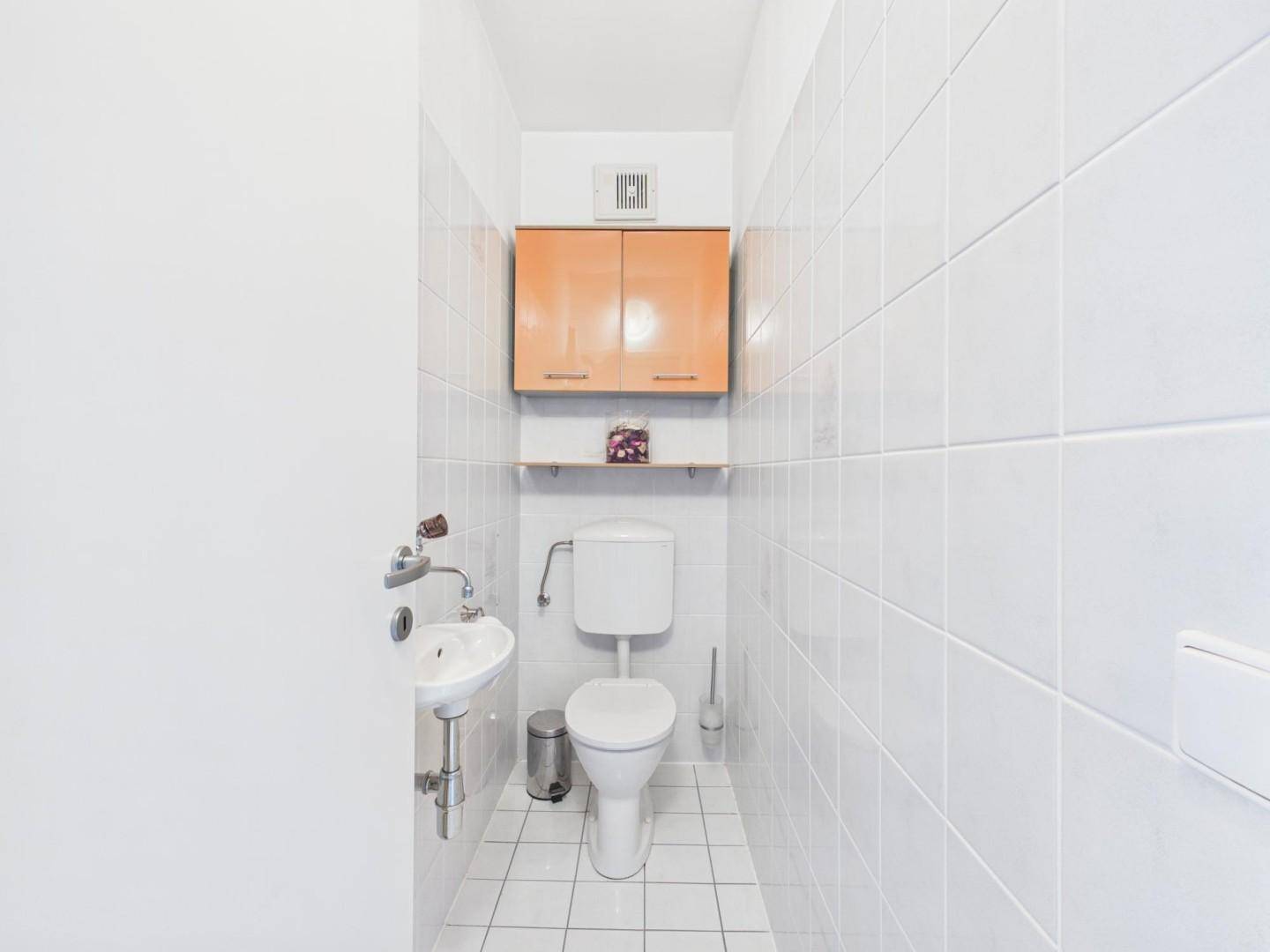 Separates Gäste-WC mit weißen Fliesen, Toilette und kleinem Waschbecken.