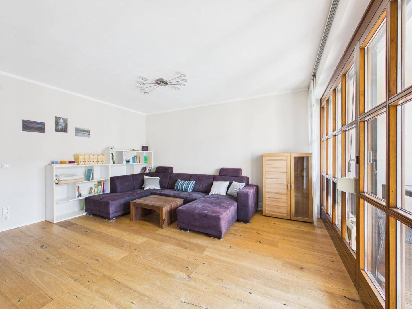 Geräumiges Wohnzimmer mit Holzboden und großen Fenstern, die viel Tageslicht hereinlassen.
