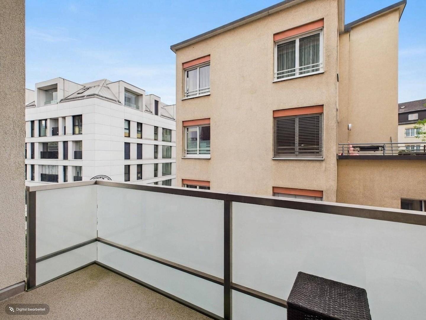 Balkon mit Glasgeländer und Blick auf die umliegenden Gebäude in der Stadt.