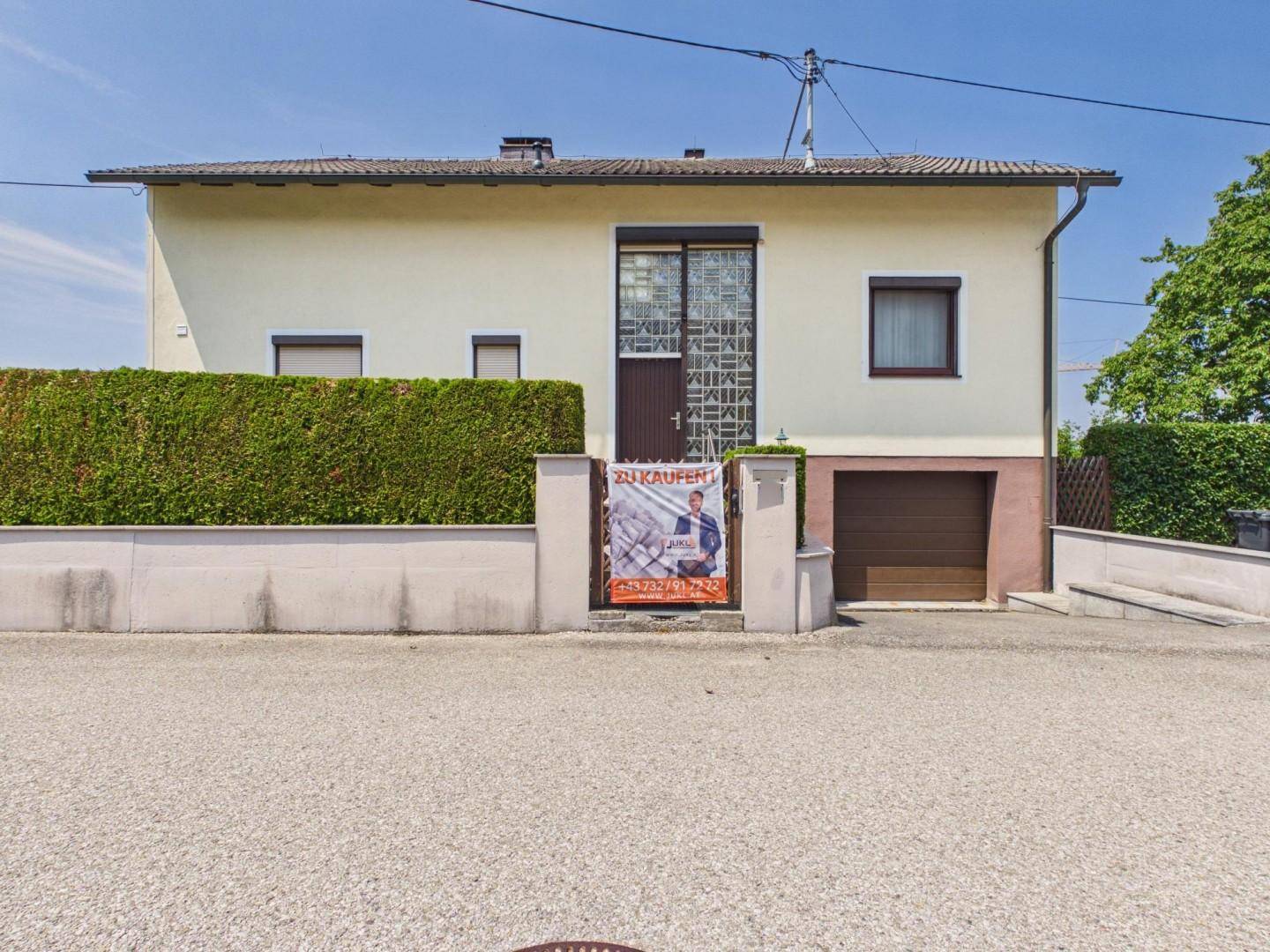 Vorderansicht eines Hauses mit Hecke, Einfahrt und Garagentor.