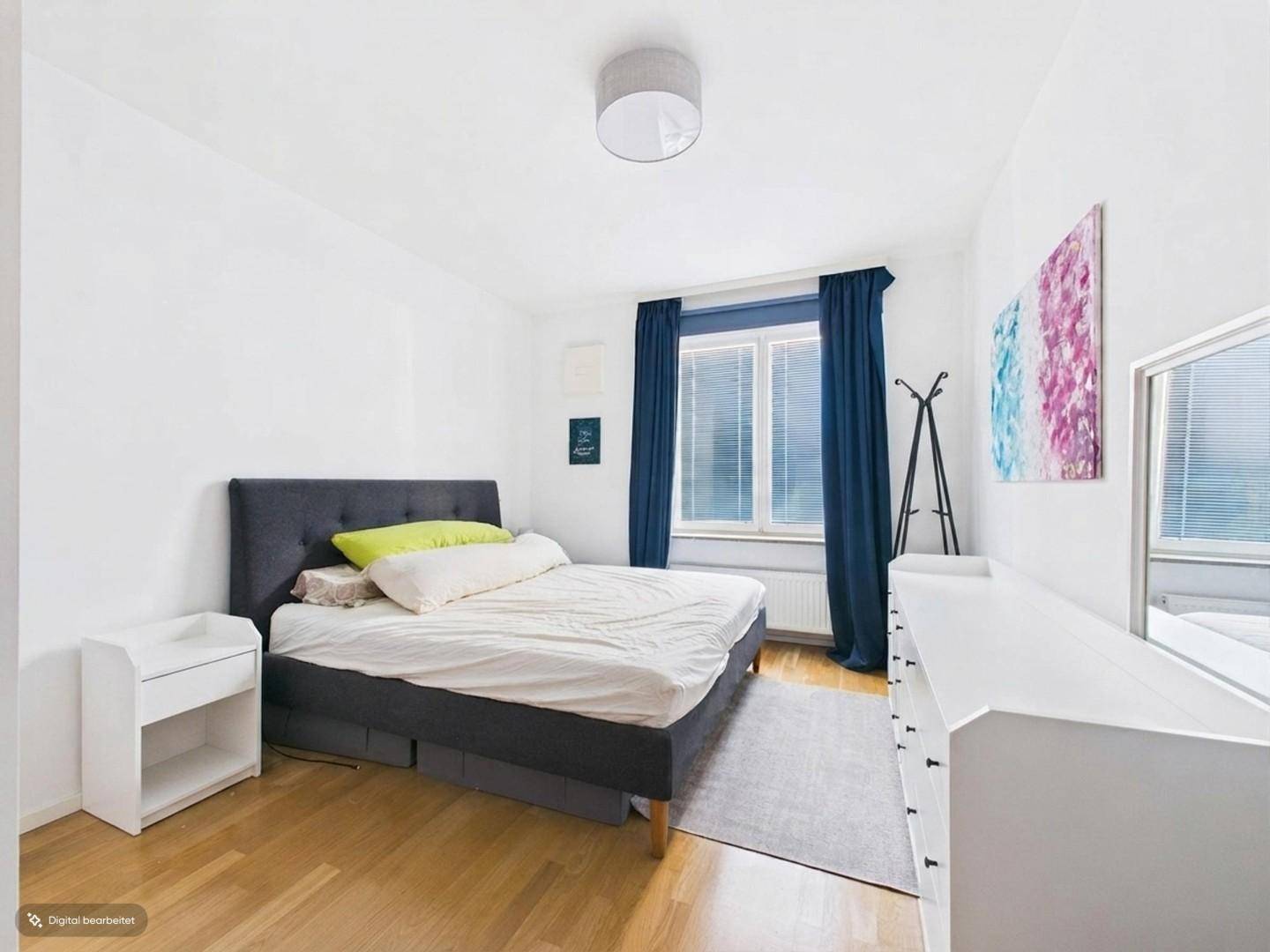 Gemütliches Schlafzimmer mit Holzboden, Doppelbett und blauen Vorhängen am Fenster.