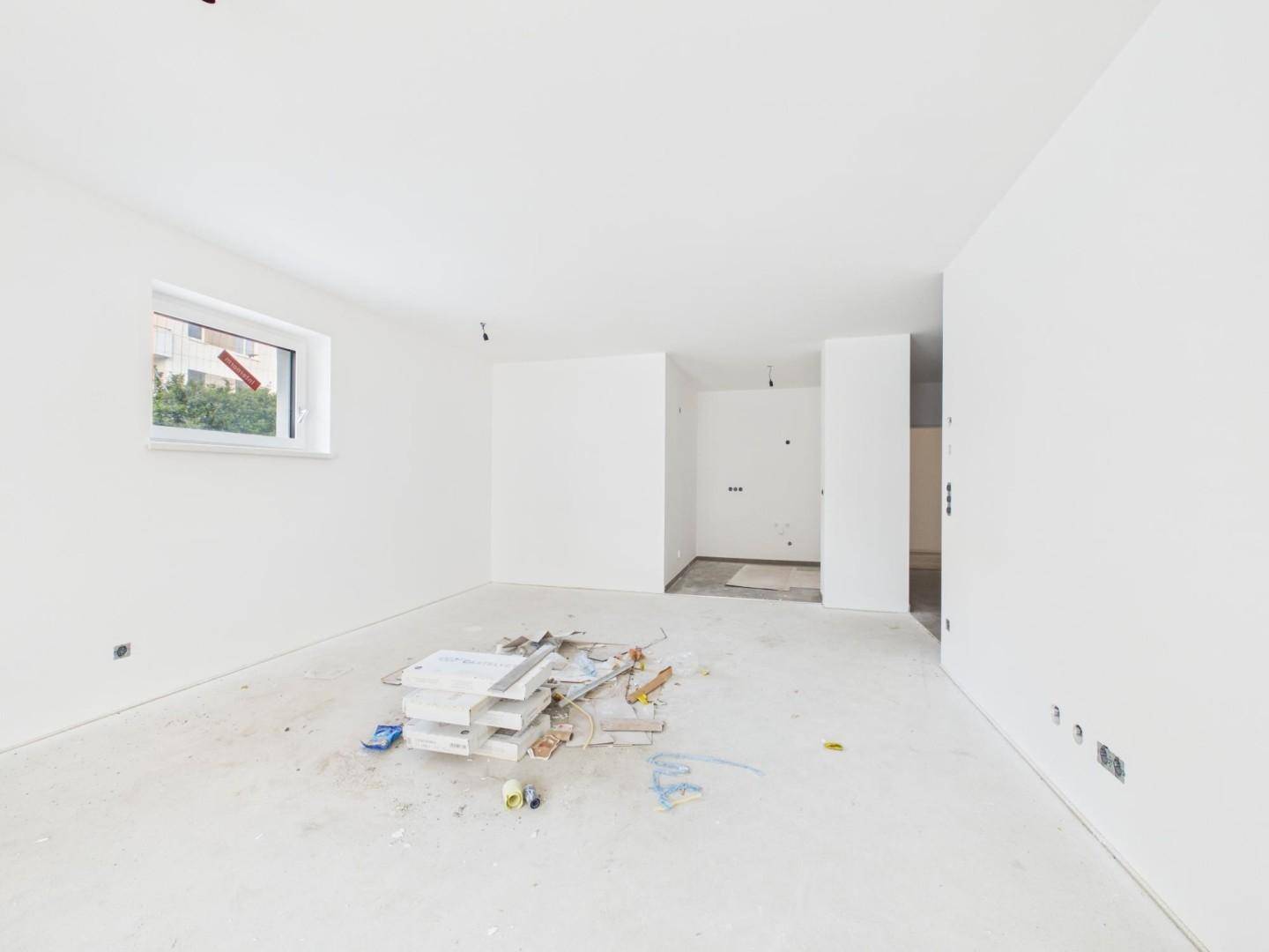 Geräumiger, unfertiger Innenraum mit viel Tageslicht und Blick auf die Baustelle.