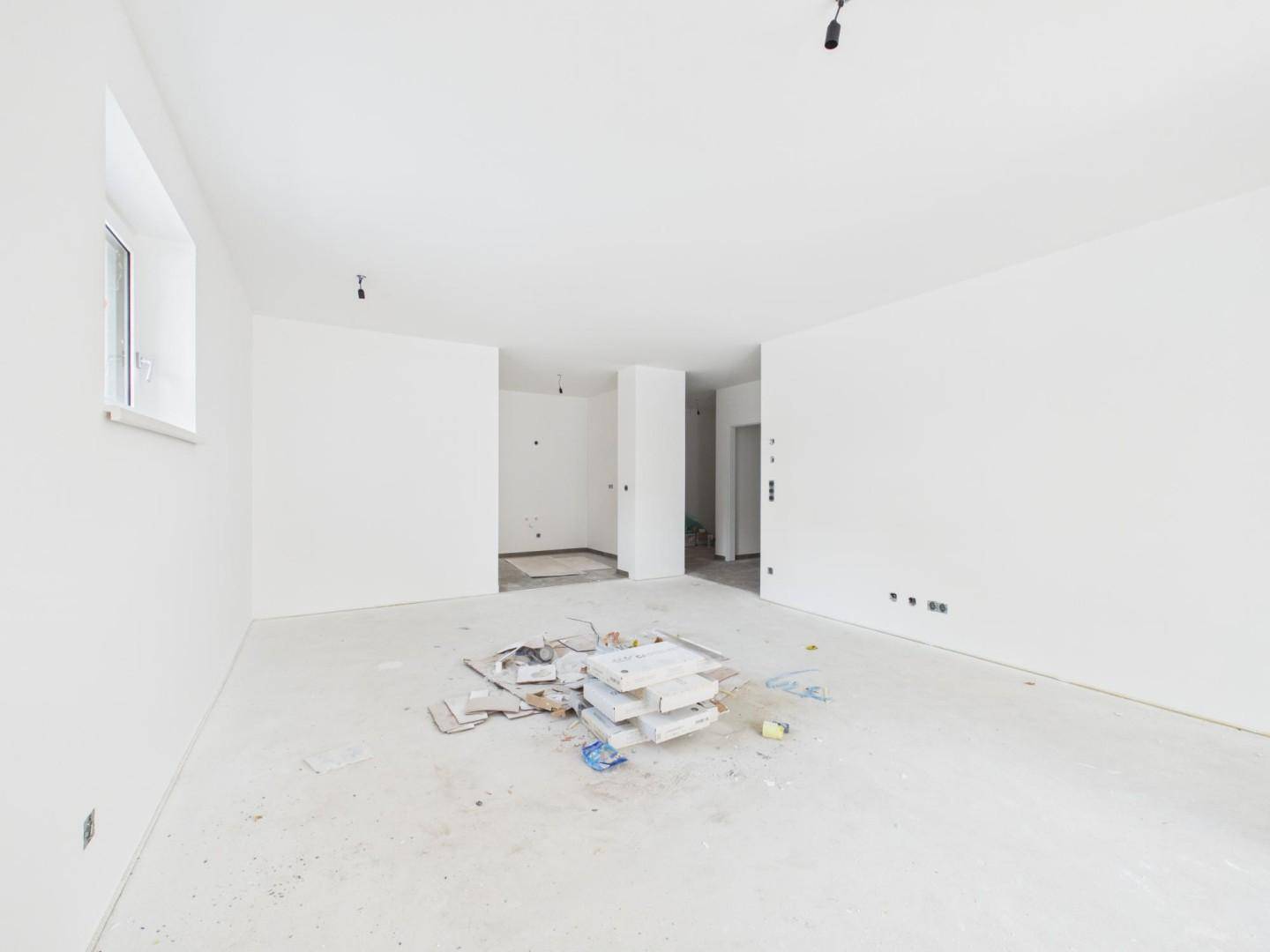 Heller, unmöblierter Raum im Rohbau mit weiß gestrichenen Wänden und Fenster.