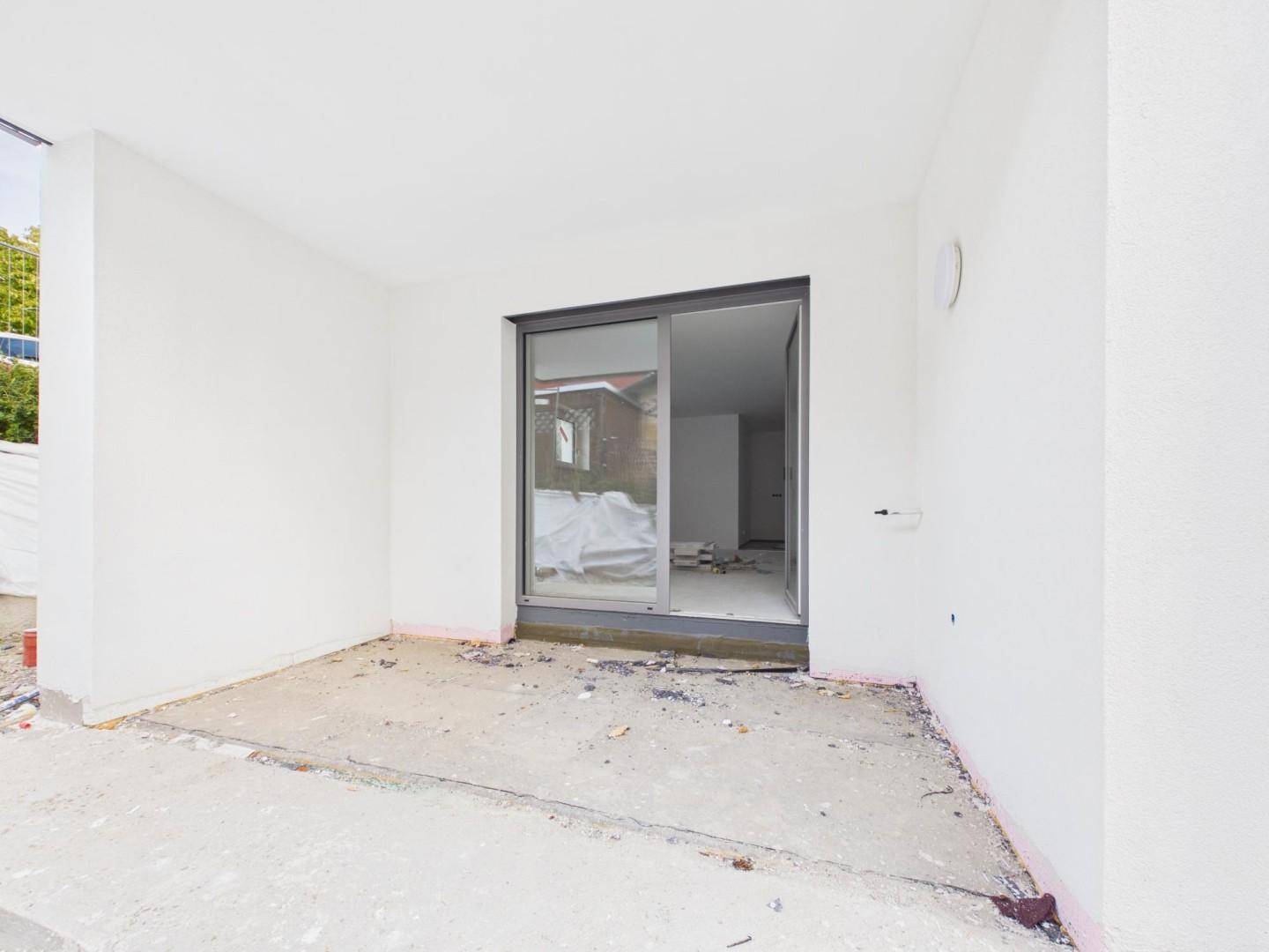 Unfertiger Balkon mit Schiebetürzugang zu einem hellen Innenraum.