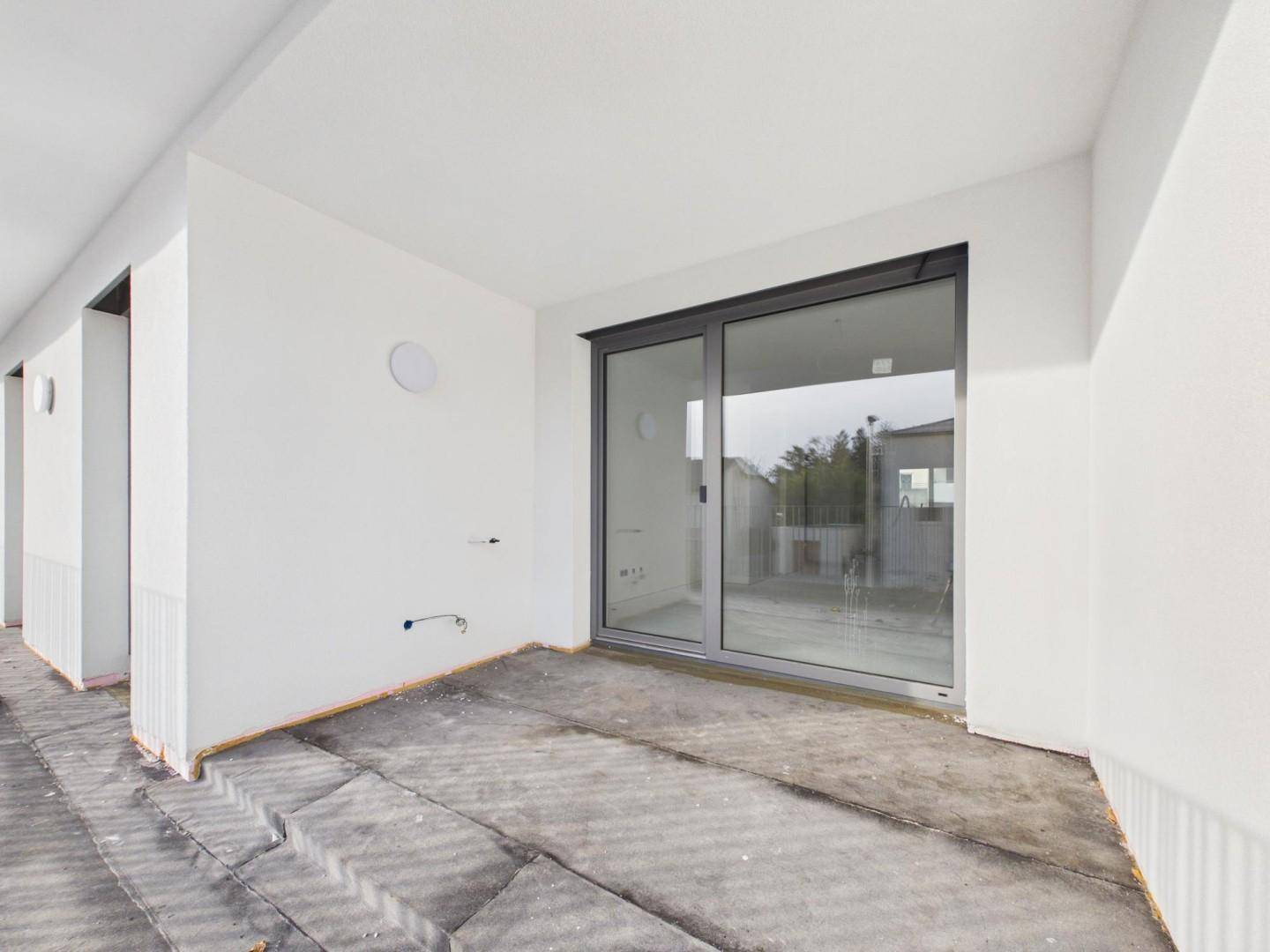 Unfertiger Balkon mit großer Glasschiebetür, die Zugang zum Innenraum des Neubaus bietet.