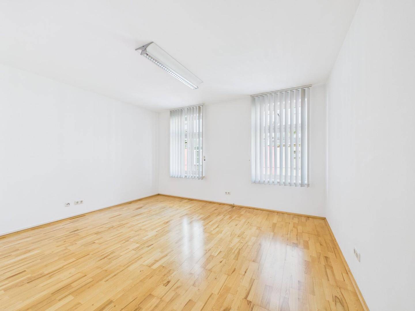 Leerer Raum mit Holzboden und großen Fenstern, vielseitig nutzbar.