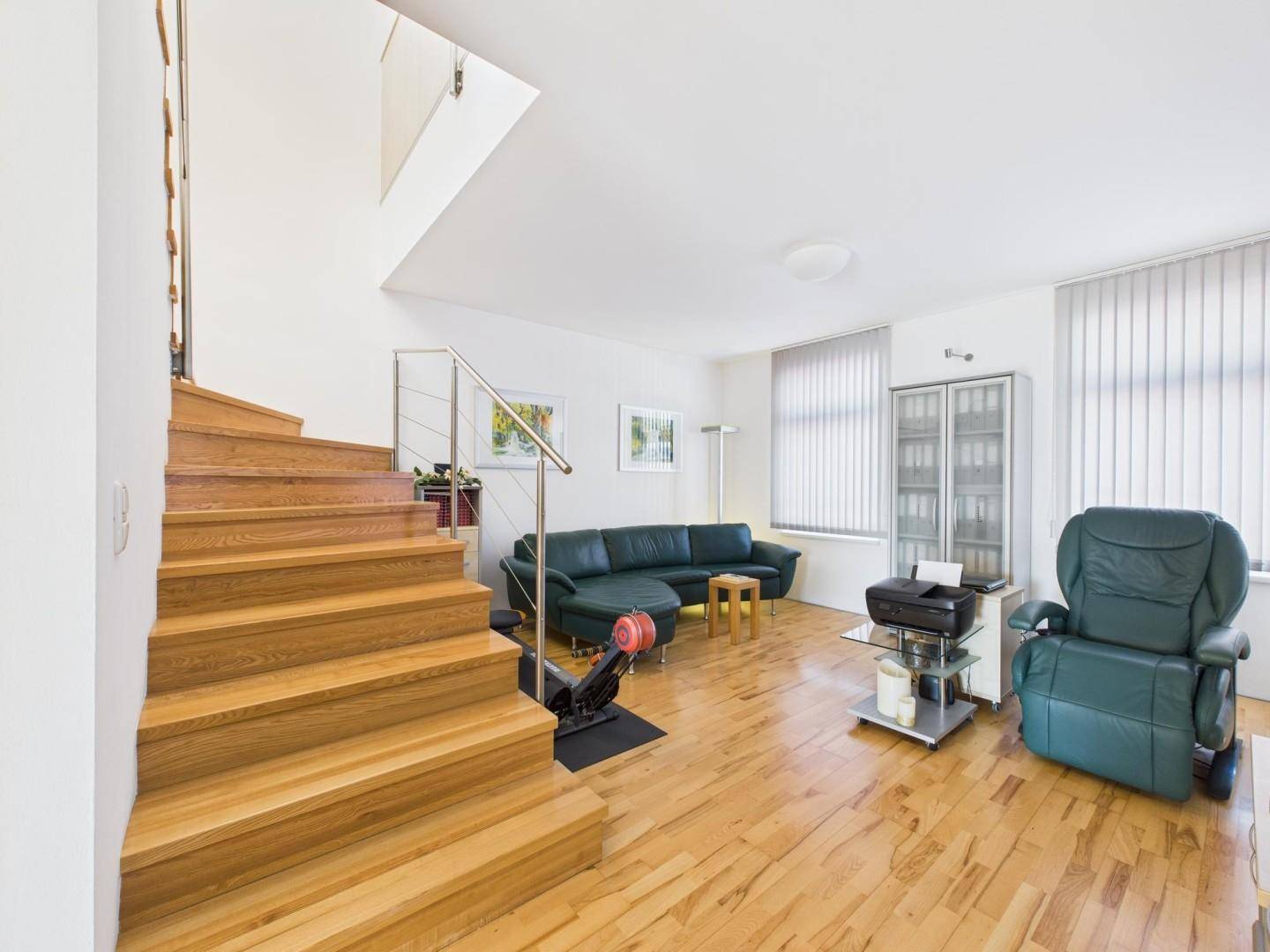 Geräumiges Wohnzimmer mit Holzboden, Ledersofa und offener Holztreppe.