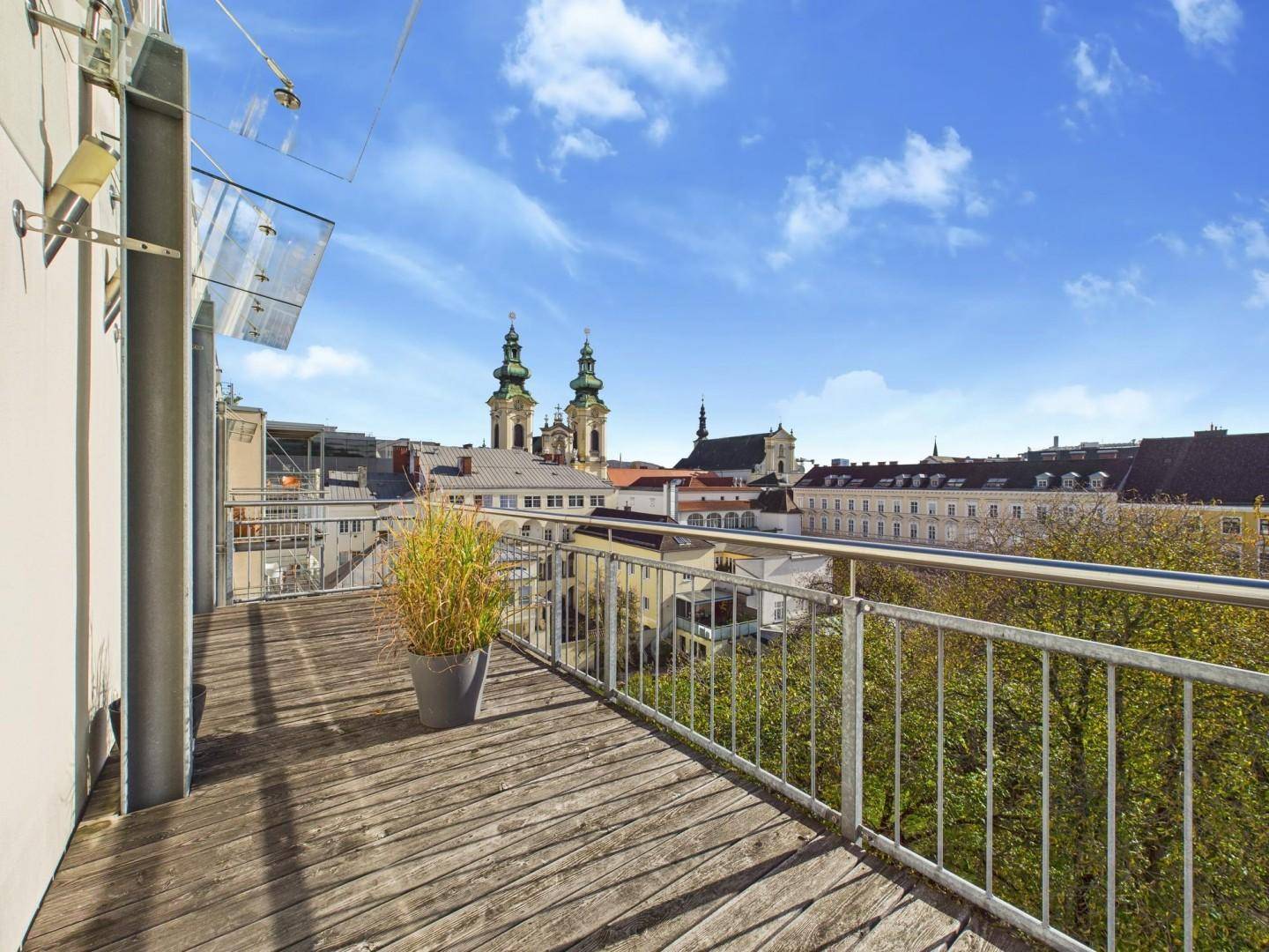 Balkon mit Holzboden und weitem Blick über die Dächer der Stadt und historische Gebäude.