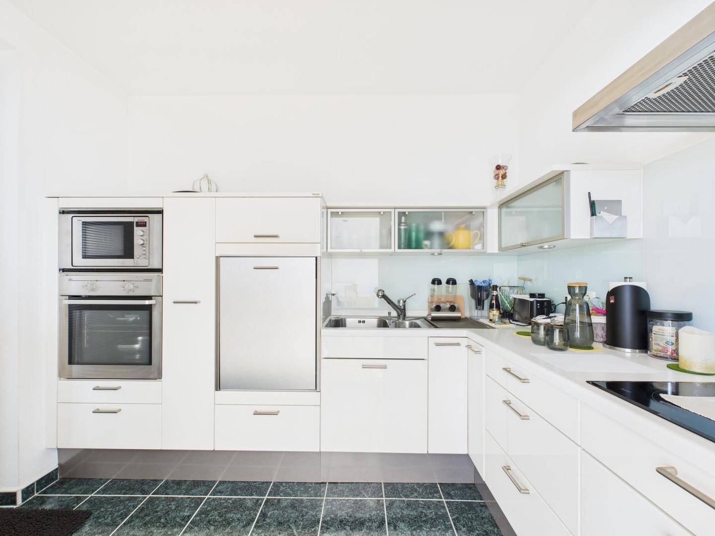 Moderne weiße Einbauküche mit integrierten Geräten und dunklem Fliesenboden.