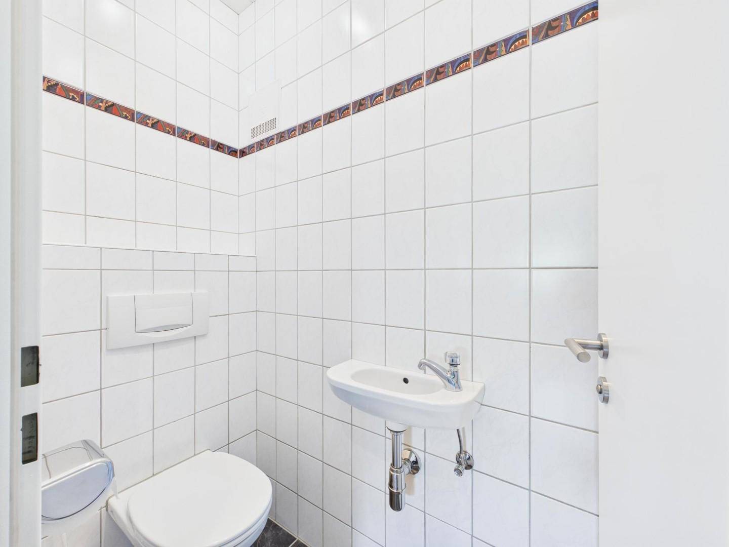 Kleines Gäste-WC mit weißen Fliesen, wandhängendem WC und einem Waschbecken.