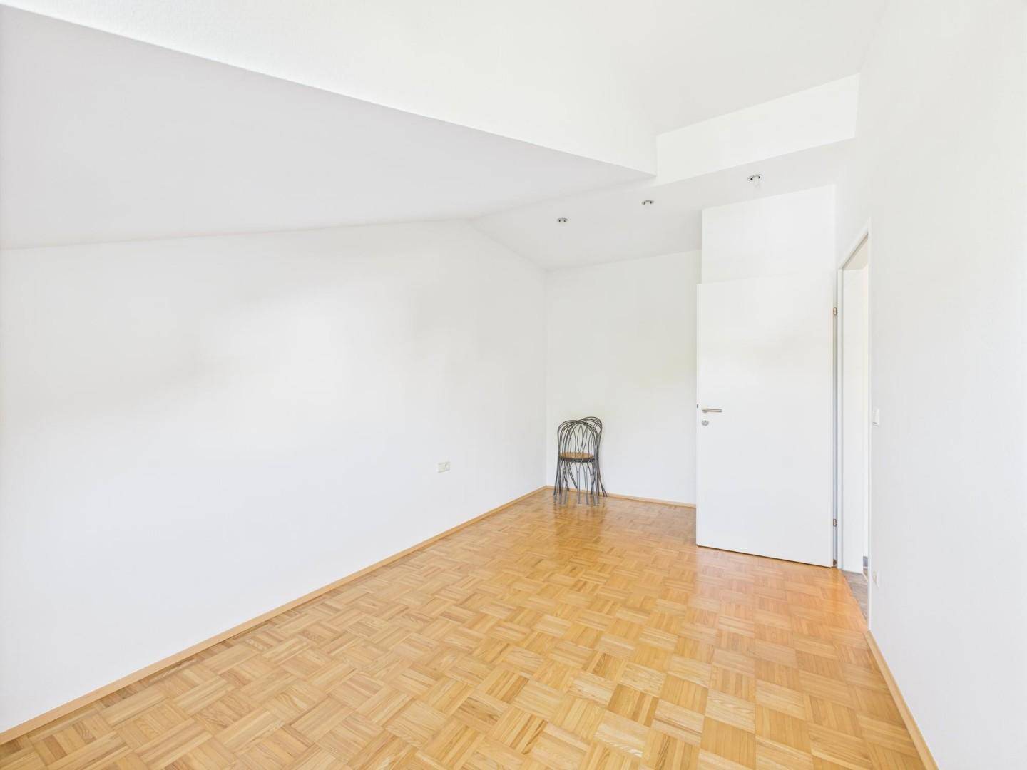Leeres Zimmer mit hellem Parkettboden und weißen Wänden, bereit zur individuellen Gestaltung.