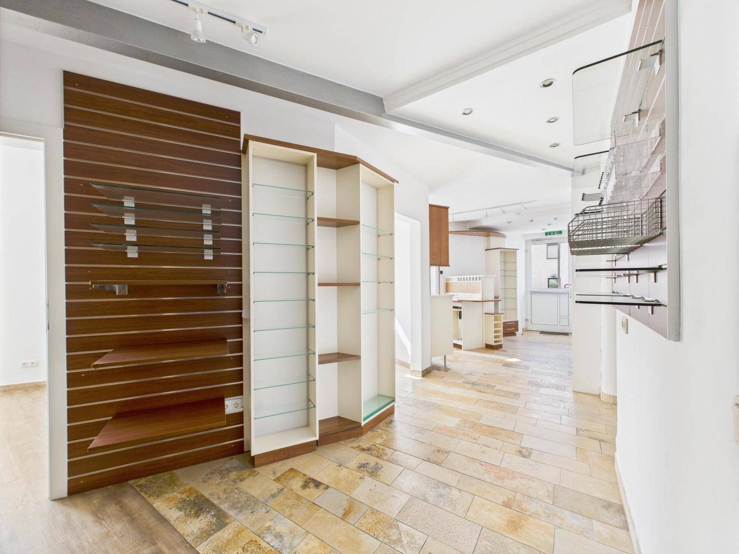 Geräumiger Ladenbereich mit Steinboden, Lamellenwand und leeren Regalen, ideal für ein Geschäft.
