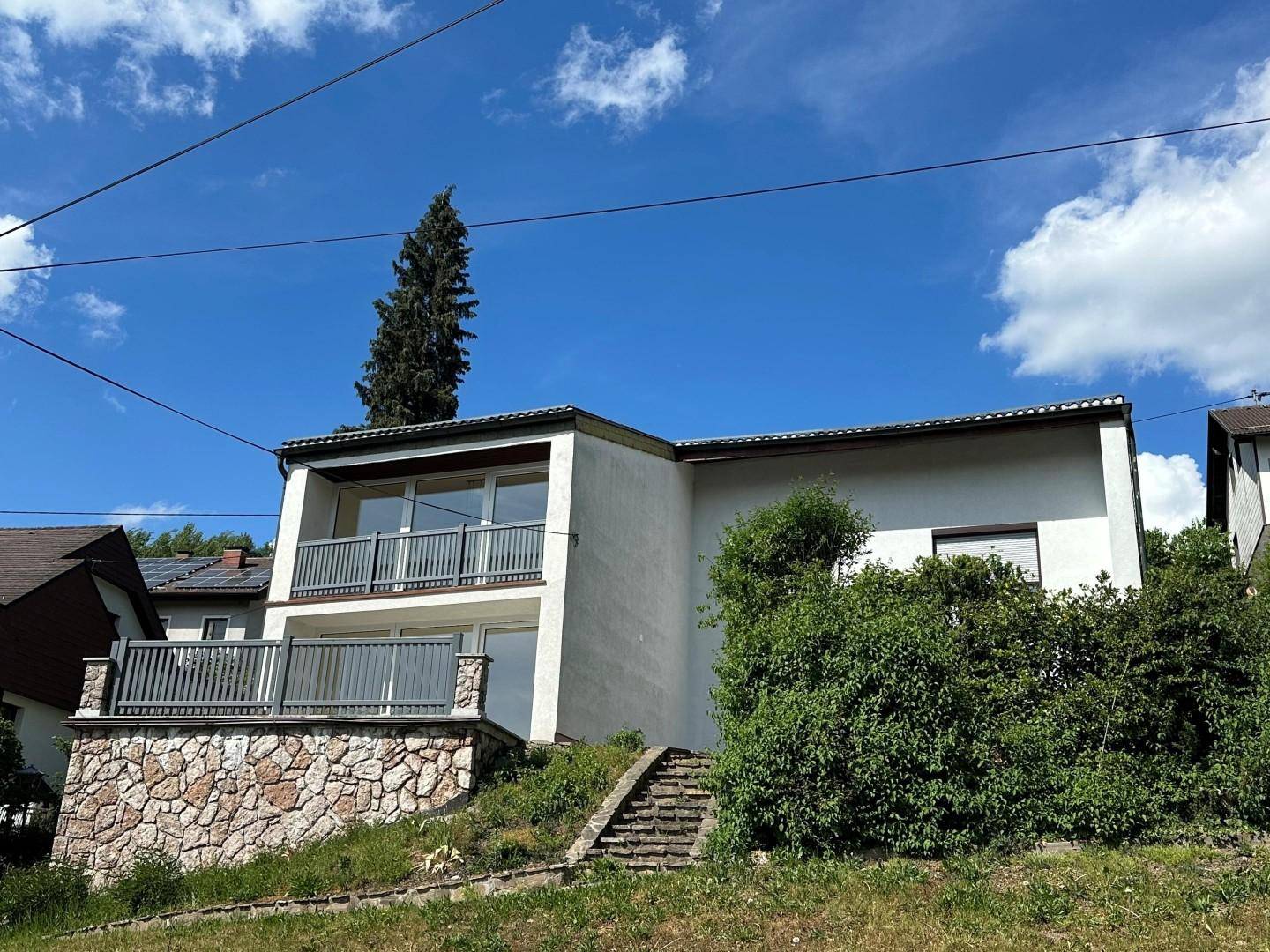 Außenansicht des Hauses mit Balkonen, Steinfassade im unteren Bereich und Treppenzugang.