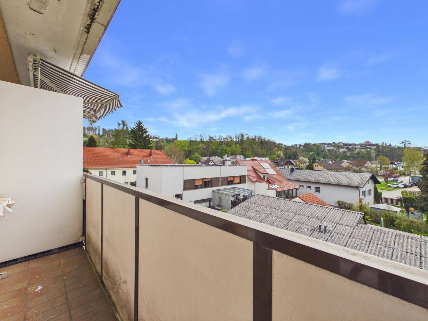 Geräumiger Balkon mit Markise und weitem Blick über die Dächer und grüne Hügel.
