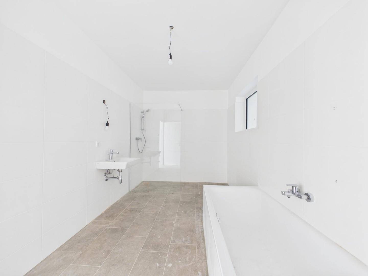 Geräumiges Badezimmer im Rohbau mit Badewanne, Dusche, Waschbecken und Fenster.