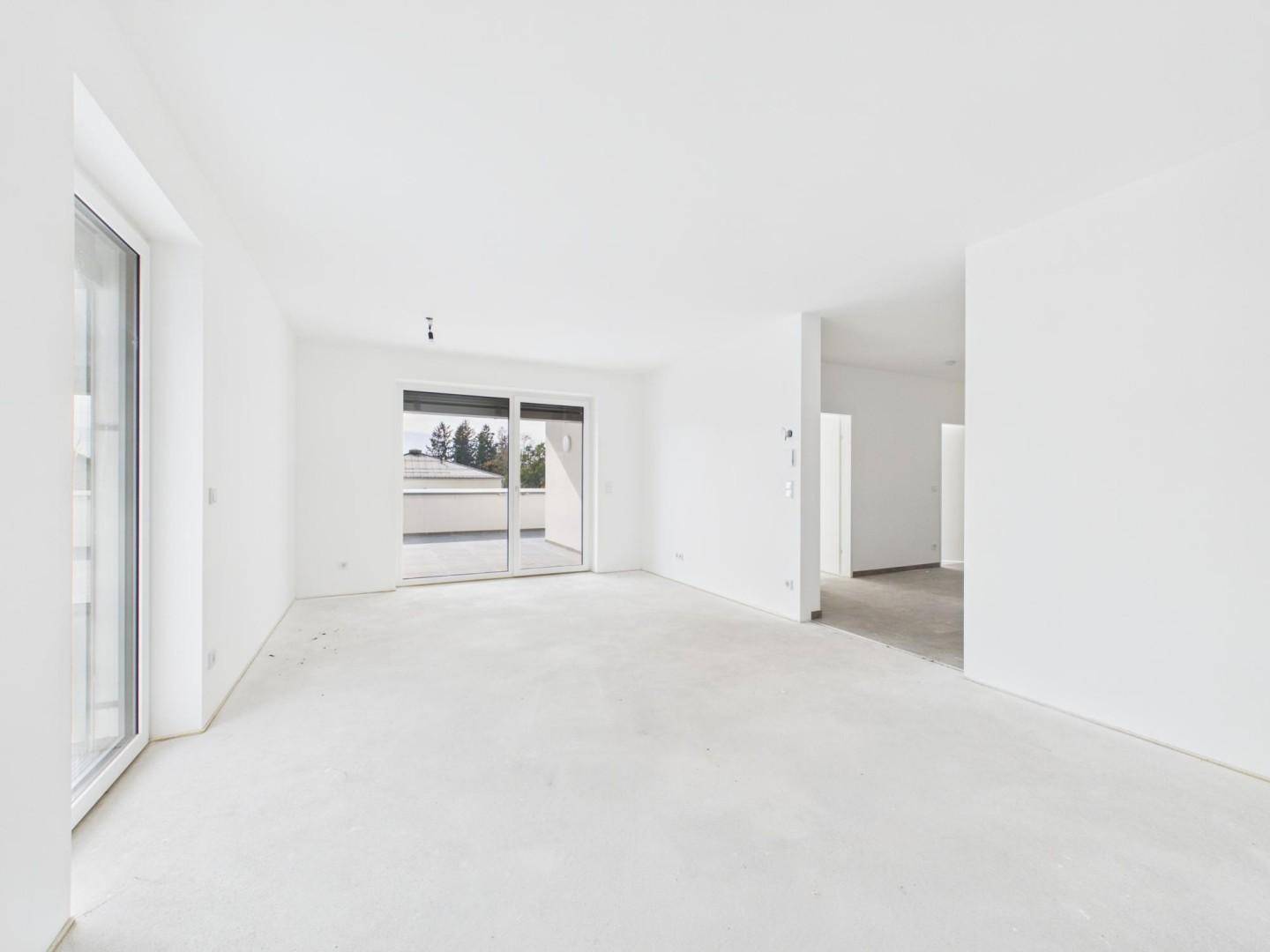 Lichtdurchfluteter Wohnraum im Rohbau mit Schiebetür zum Balkon und viel Potenzial.