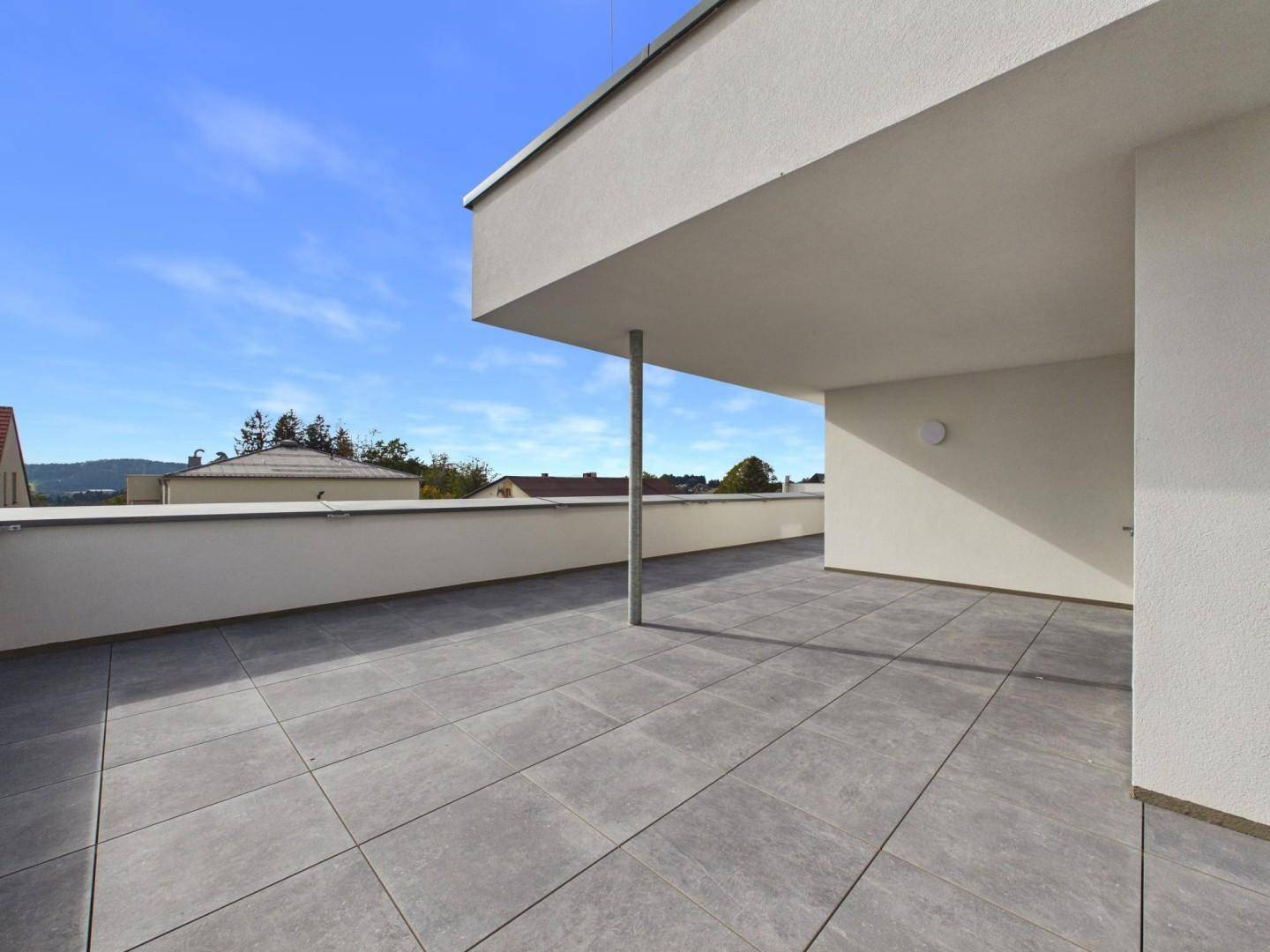 Weitläufige Dachterrasse mit grauen Fliesen und Panoramablick auf die Umgebung.