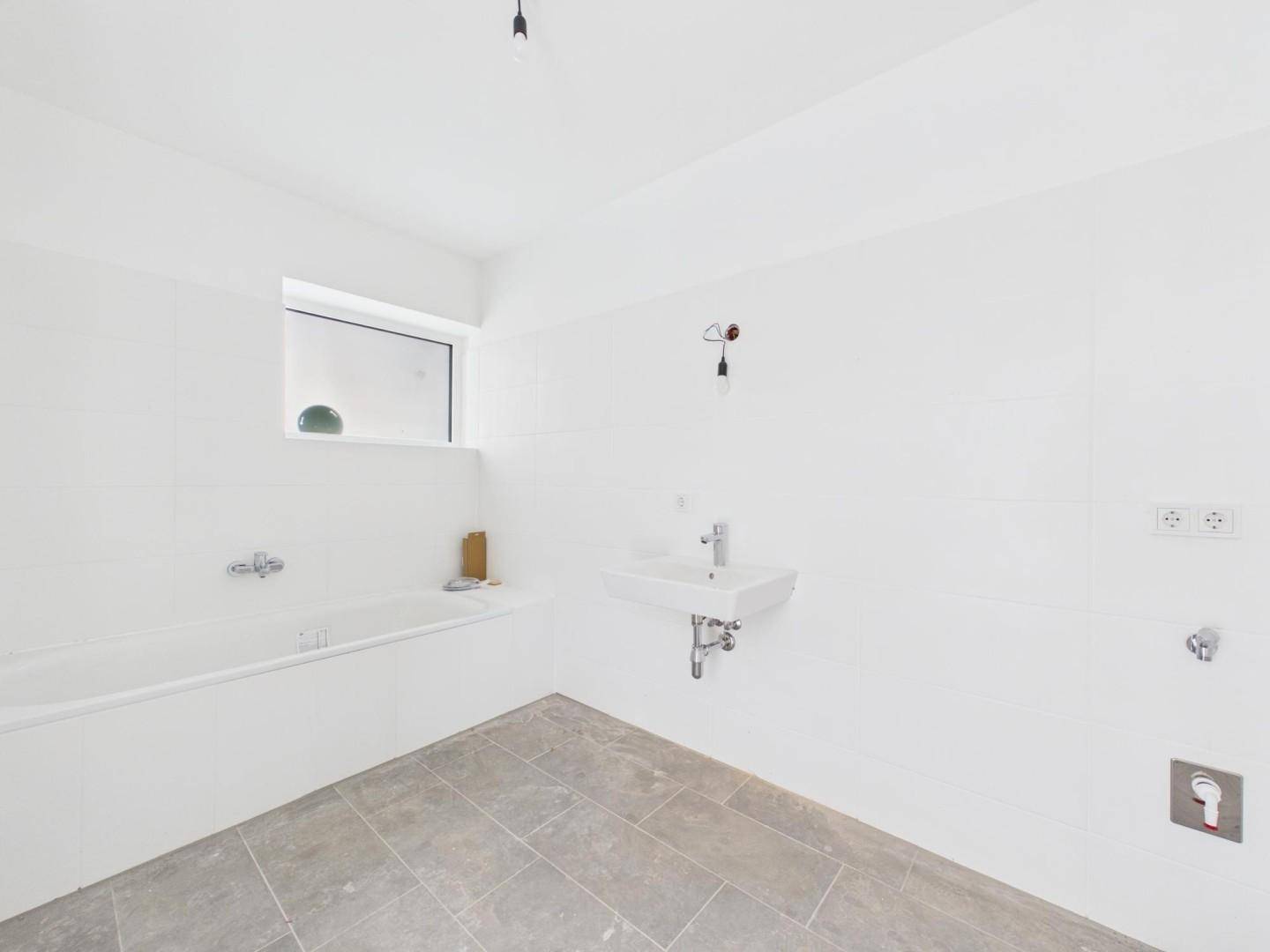 Unfertiges Badezimmer mit Badewanne, Waschbecken und Fenster, bereit für den Ausbau.