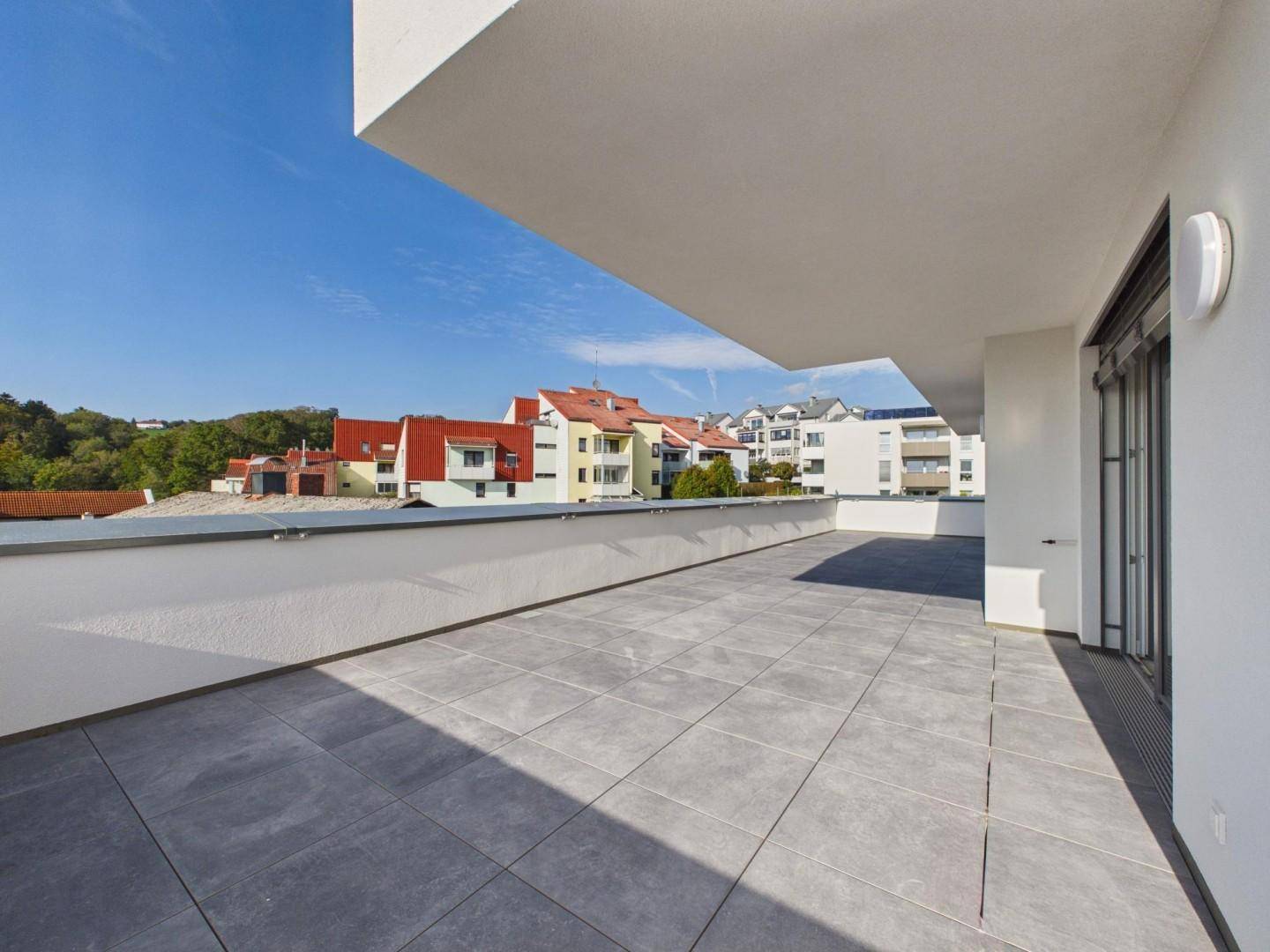Große, geflieste Terrasse mit Blick auf die umliegende Wohnbebauung und grüne Hügel.