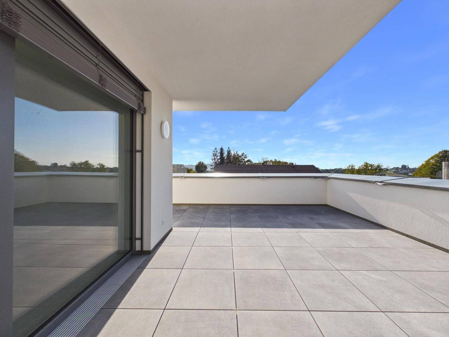 Geräumige, geflieste Terrasse mit weitem Blick in die Landschaft unter blauem Himmel.