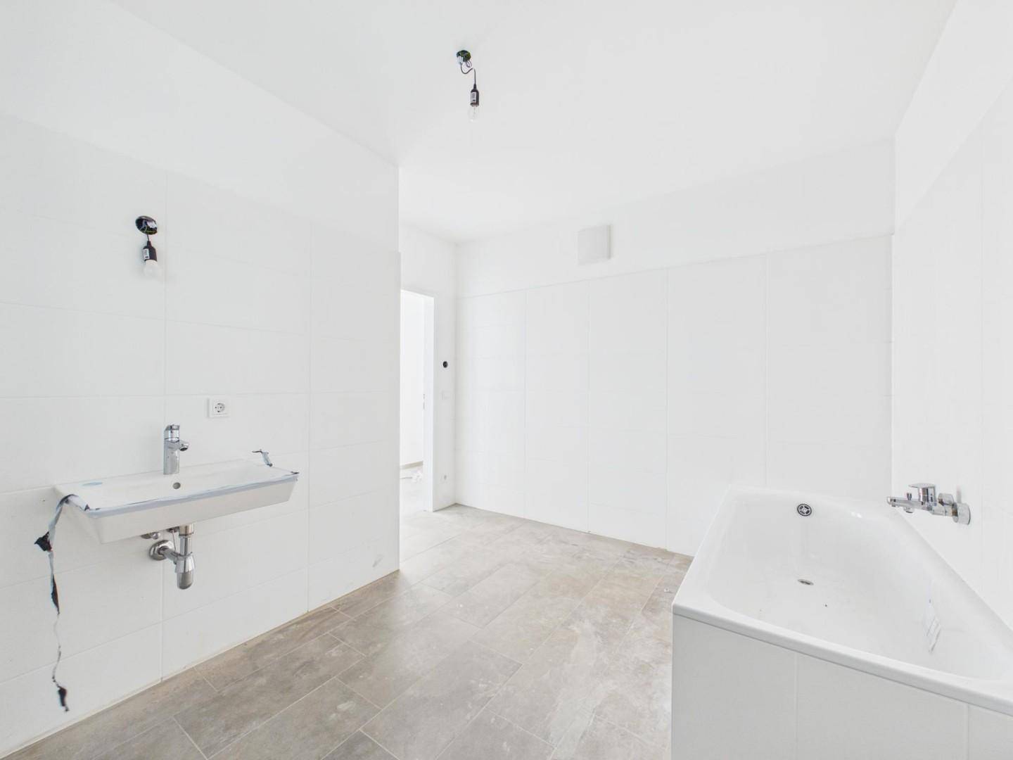 Unfertiges Badezimmer mit Badewanne und Waschbecken, bereit für die Endmontage der Armaturen.