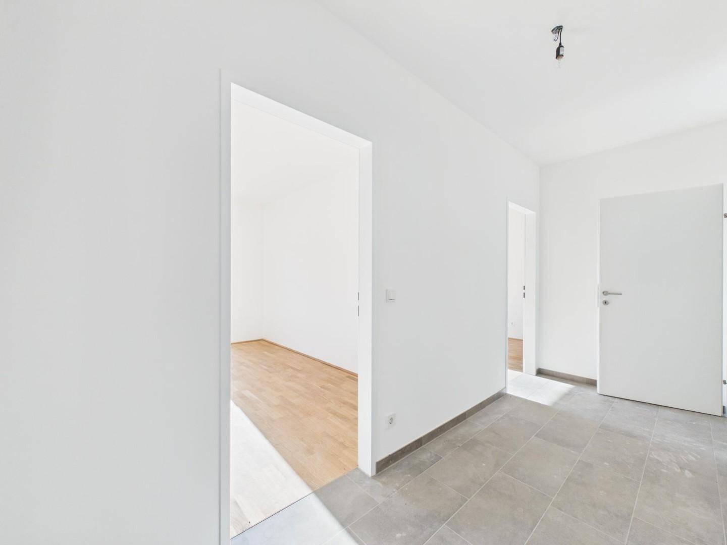 Übergangsbereich von einem gefliesten Flur zu einem Zimmer mit hellem Parkettboden und viel Tageslicht.