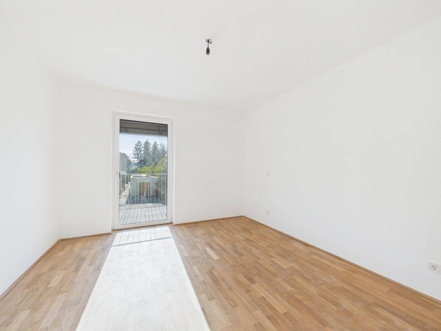 Helles Schlafzimmer mit Parkettboden und direktem Zugang zu einem Balkon, bietet viel Tageslicht.