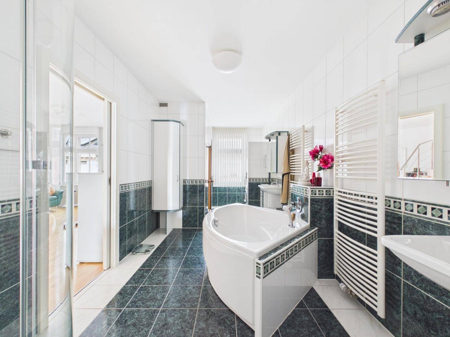 Geräumiges Badezimmer mit Eckbadewanne, Dusche und dunkelgrünen Fliesen.