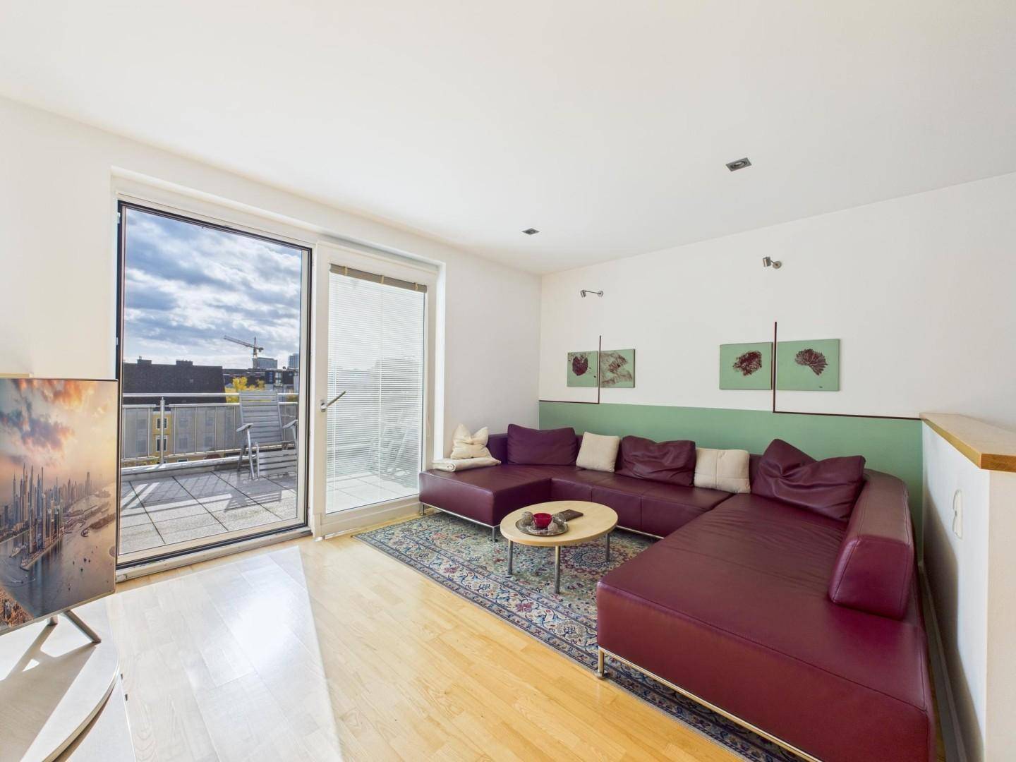 Helles Wohnzimmer mit Holzboden, bequemer Couch und Zugang zu einem Balkon.