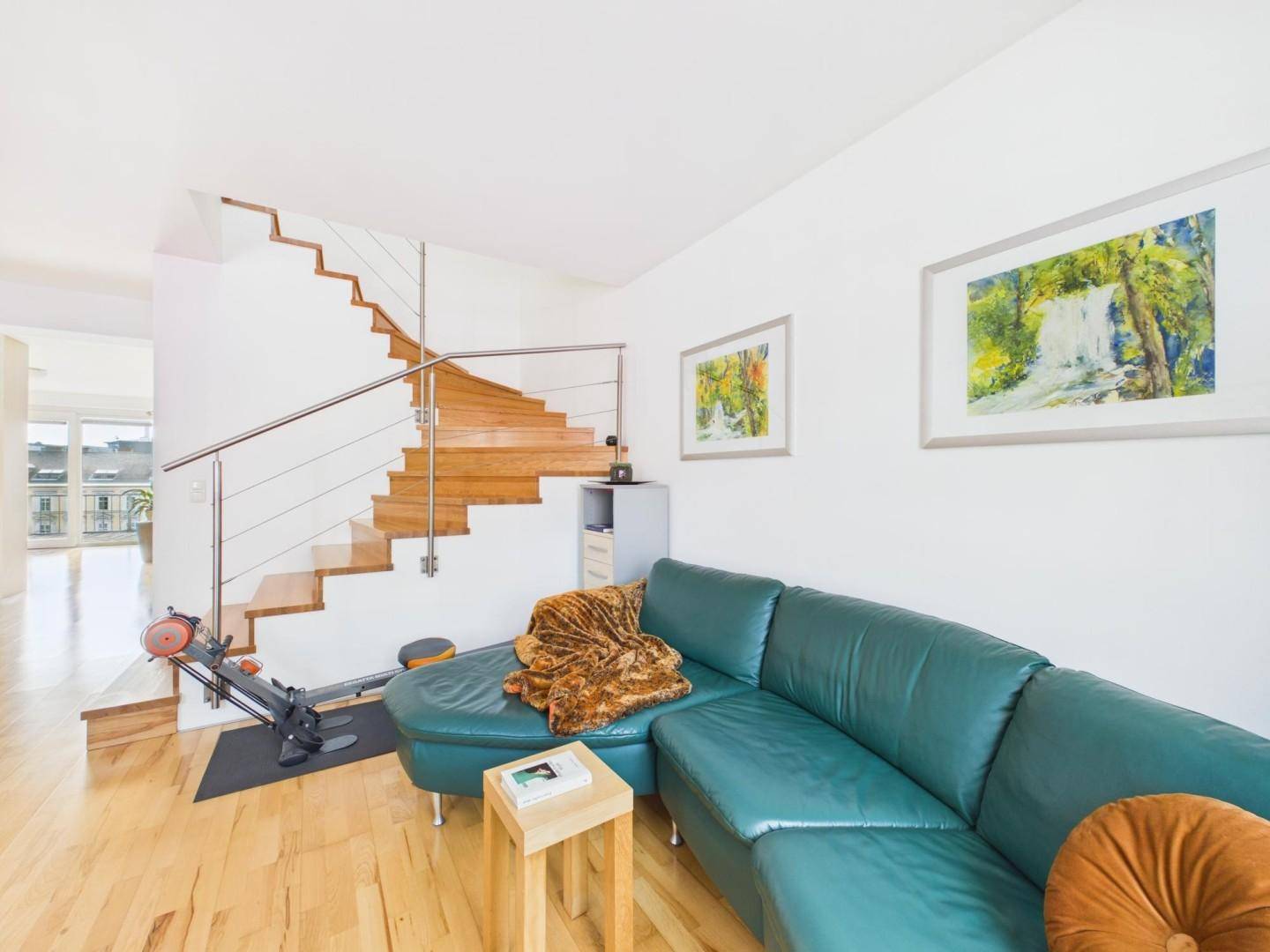 Heller Wohnbereich mit Holzboden, moderner Treppe und bequemer Ledercouch.