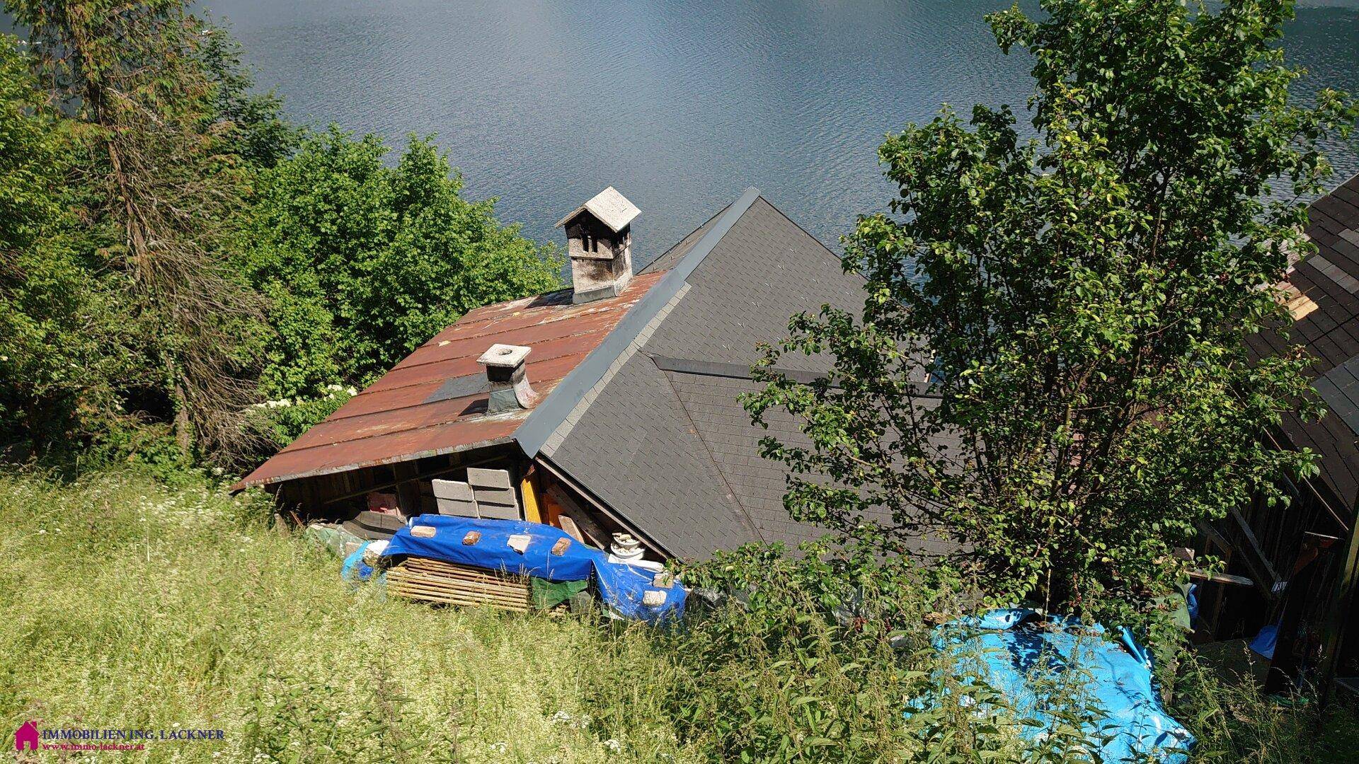 Dächer von Häusern am Hang mit Blick auf den ruhigen See und die Berge.
