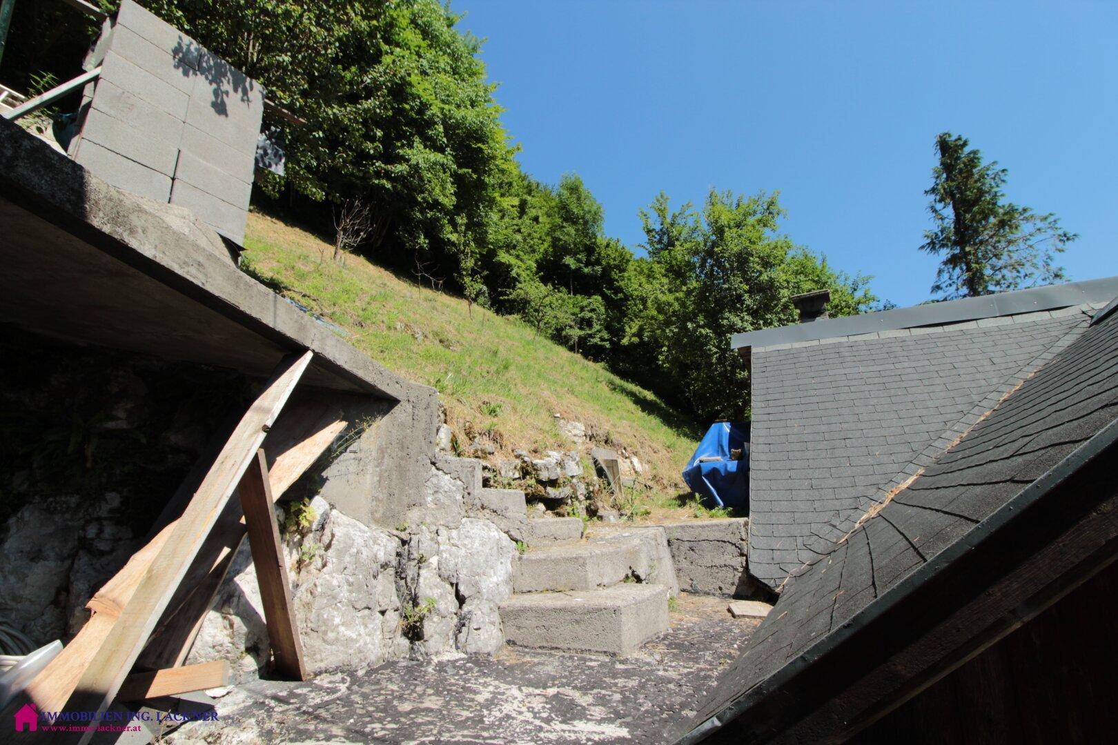 Betonierte Terrasse am Hang mit Blick auf die bewaldete Umgebung und ein Dach.