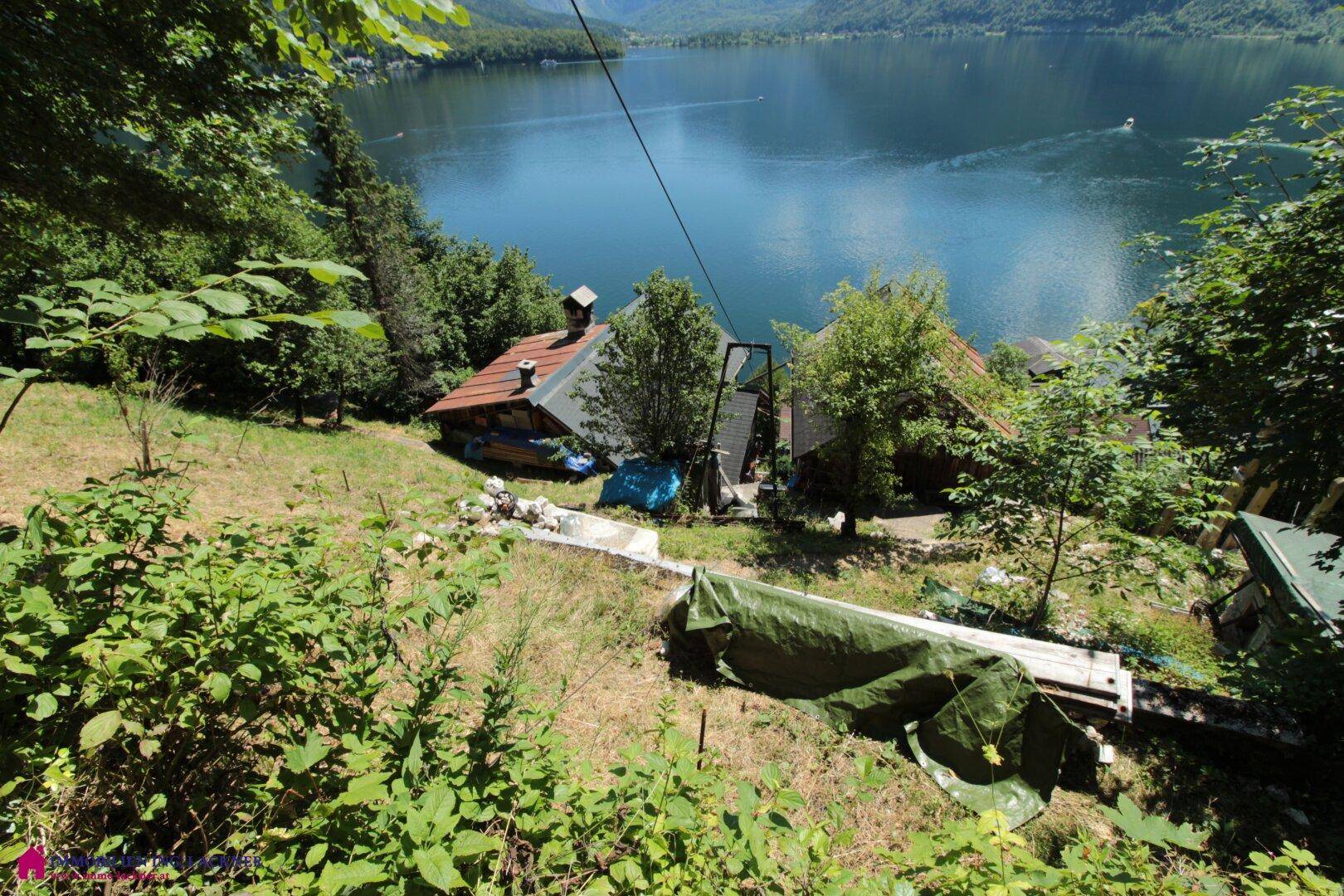 Steiler Grashang mit Häusern und dem See im Hintergrund, umgeben von Natur.