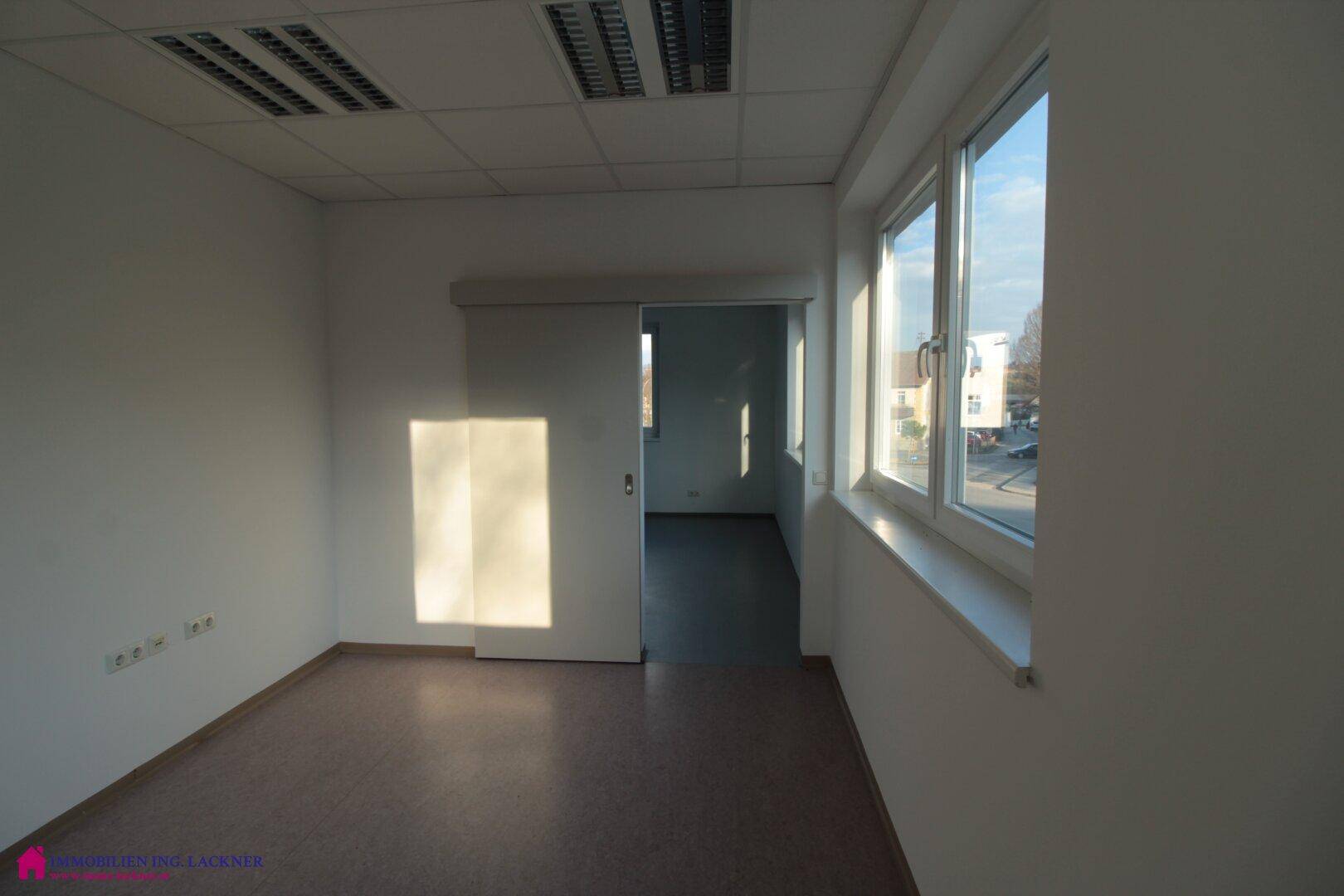 Helles Büro mit Schiebetür, großen Fenstern und Blick auf die Umgebung.