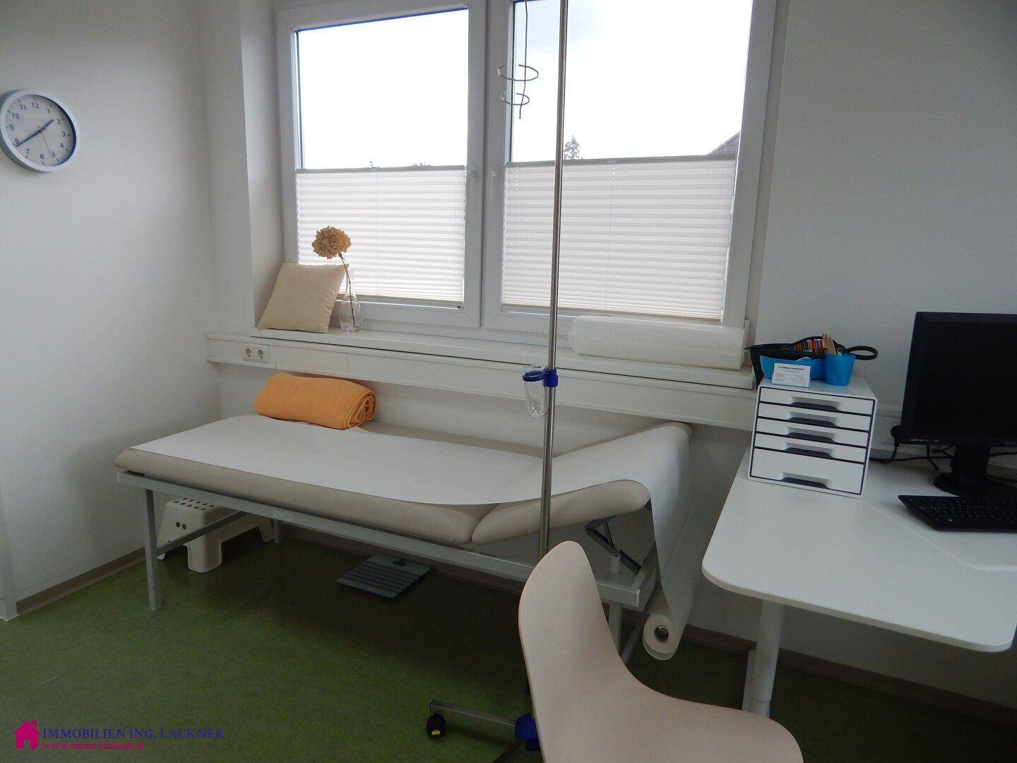 Heller Behandlungsraum mit Liege, Infusionsständer und Fenster mit Jalousien.
