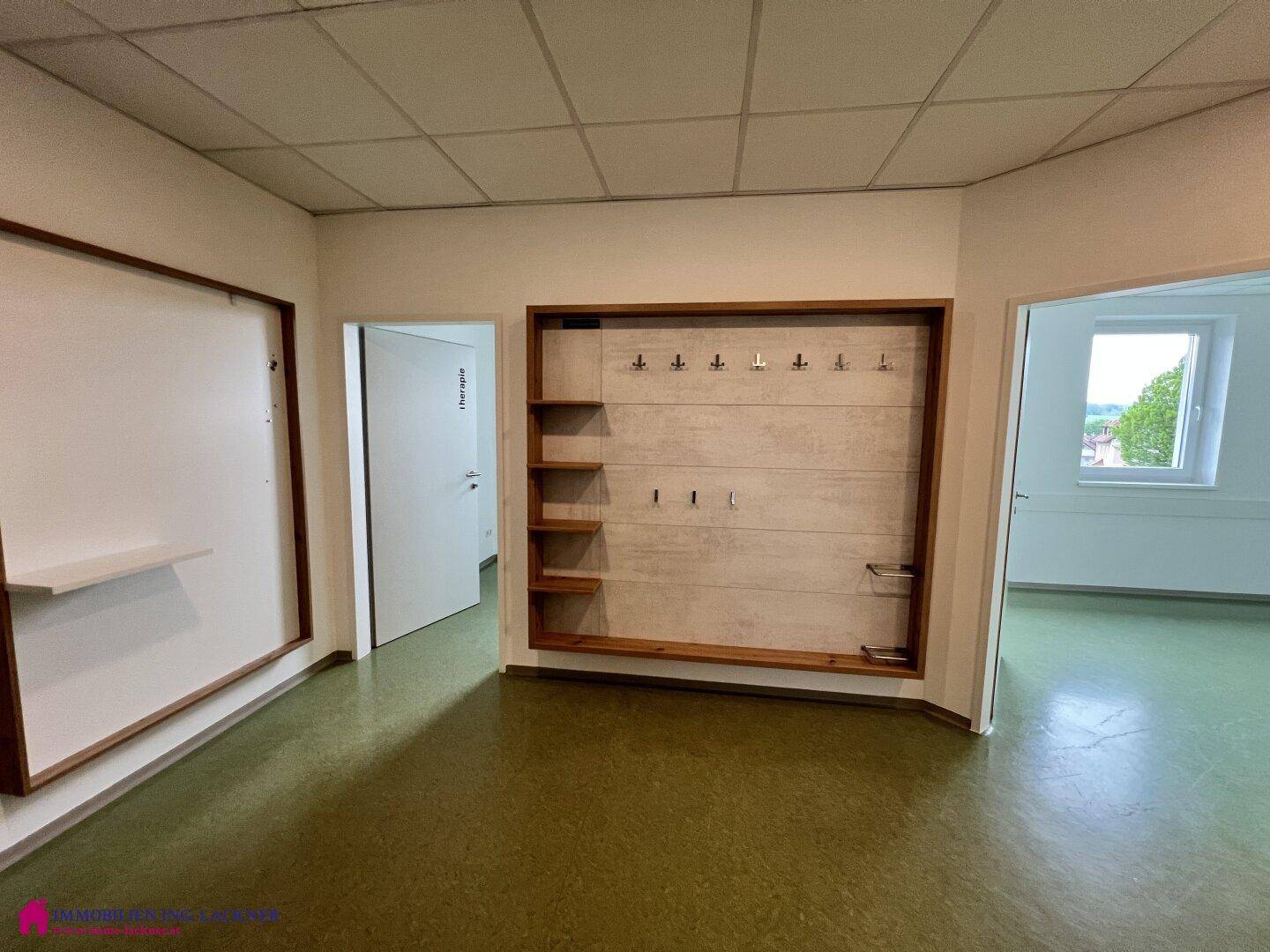 Geräumiger Büroraum mit grünem Linoleumboden und einer eingebauten Garderobe mit Holzregalen.