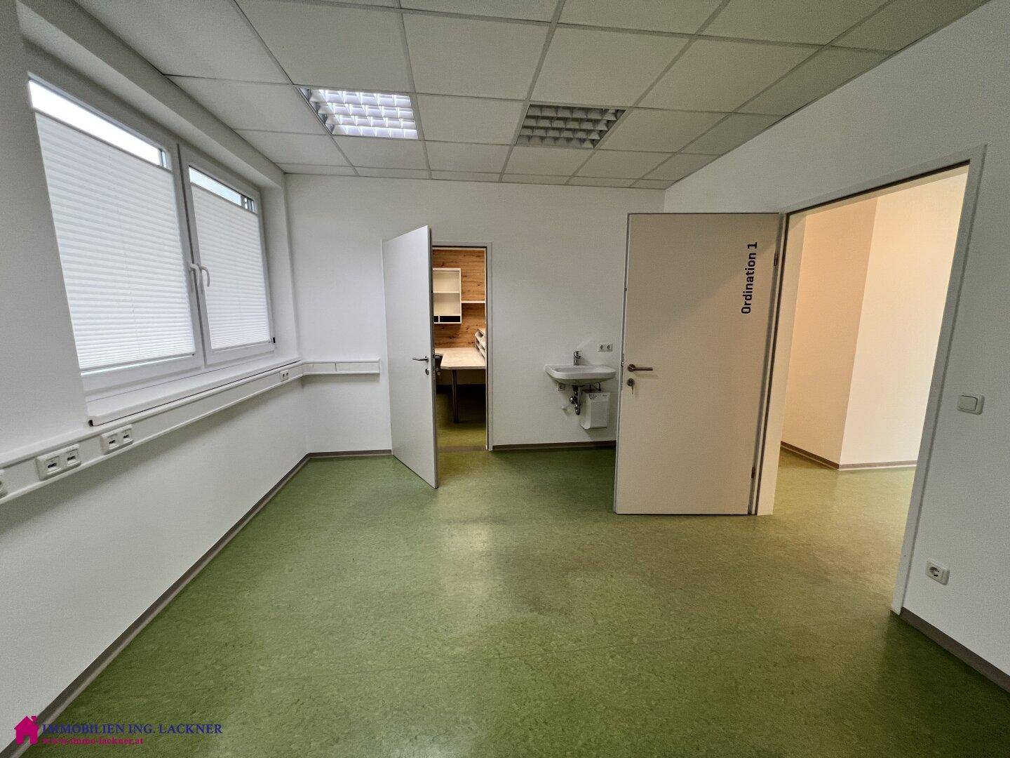 Büroraum mit grünem Linoleumboden, Waschbecken und Zugang zu weiteren Räumen, ideal für eine Praxis.