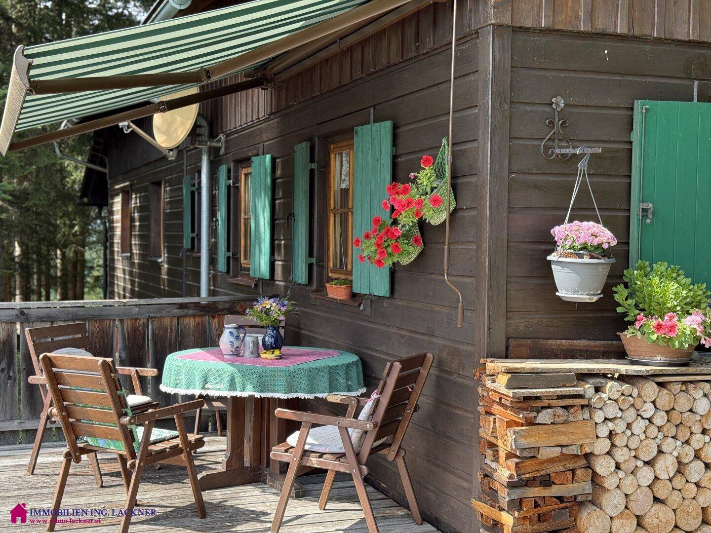 Traditionelles Holzhaus mit gestreifter Markise, gemütlichem Essbereich im Freien und Holzstapel.