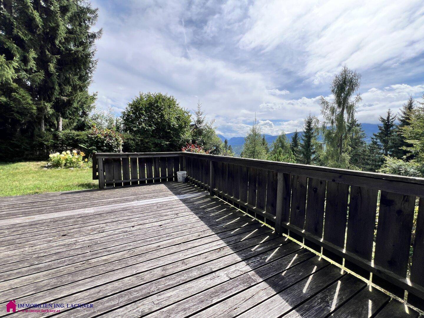 Weitläufige Holzterrasse mit rustikalem Geländer und Panoramablick auf die grüne Bergwelt.
