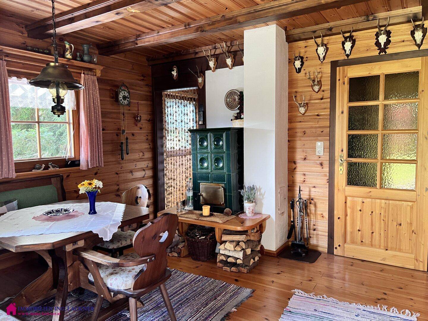 Rustikaler Wohn-Essbereich mit Holzbalkendecke, Kachelofen und traditionellen Jagdtrophäen an den Wänden.