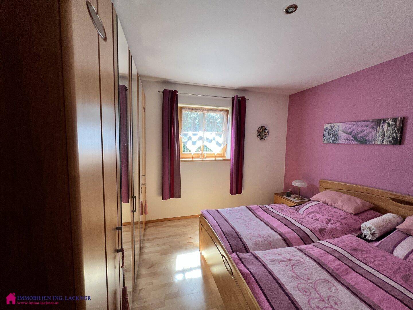 Gemütliches Schlafzimmer mit zwei Einzelbetten, lila Wänden und einem großen Holzschrank.