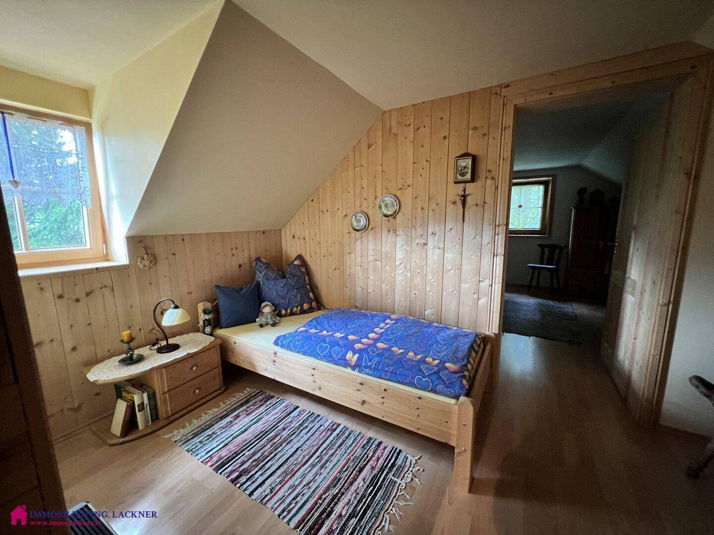 Helles Dachgeschoss-Schlafzimmer mit Holzwänden, Einzelbett und Fenster für natürlichen Lichteinfall.