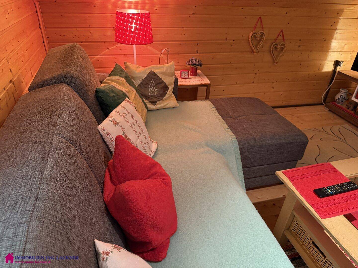 Detailansicht der bequemen Couch im Wohnzimmer mit farbenfrohen Kissen und einer roten Lampe.