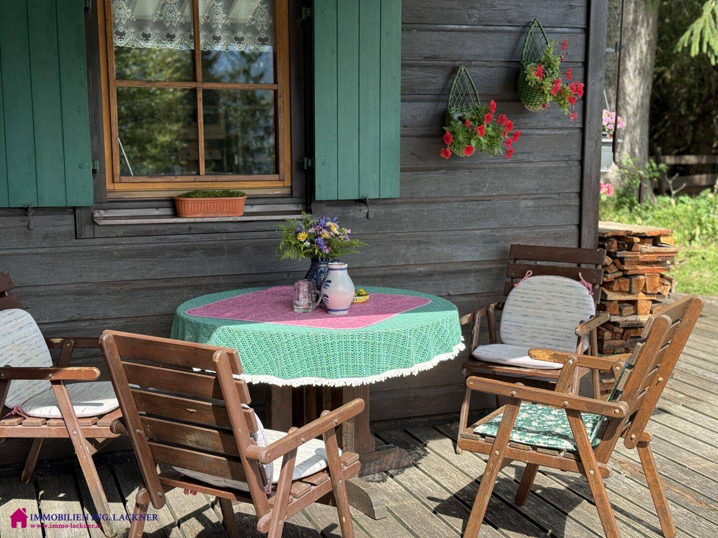 Idyllischer Außenbereich mit Holztisch und Stühlen, umgeben von Blumen und der rustikalen Hausfassade.