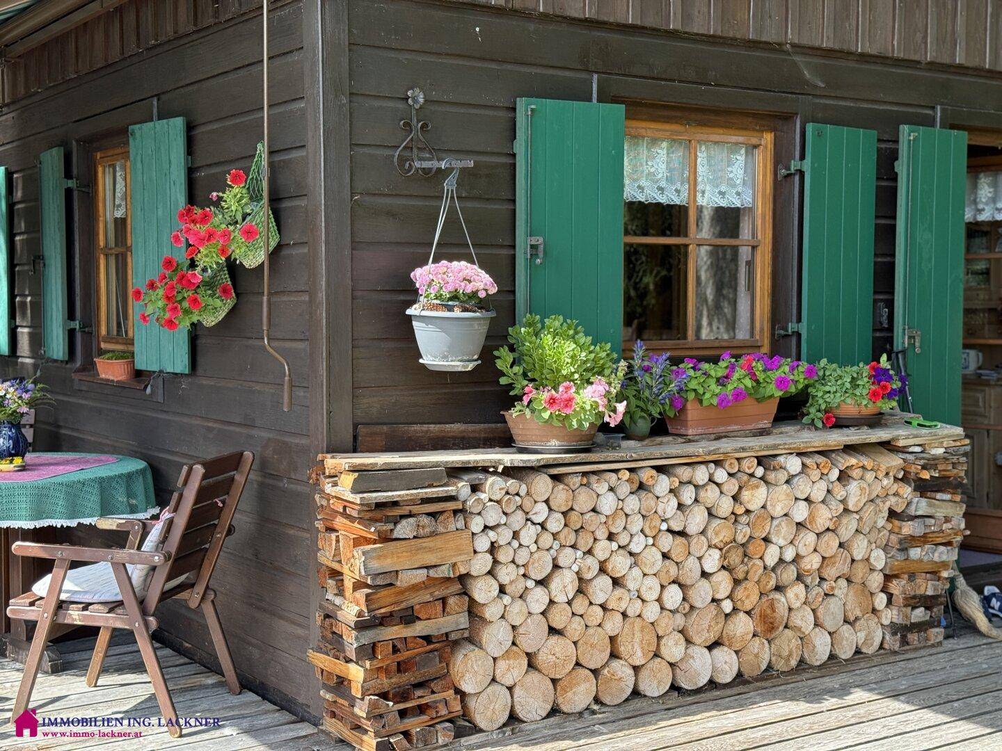 Gemütliche Ecke des Holzhauses mit grünen Fensterläden und einem dekorativen Holzstapel.